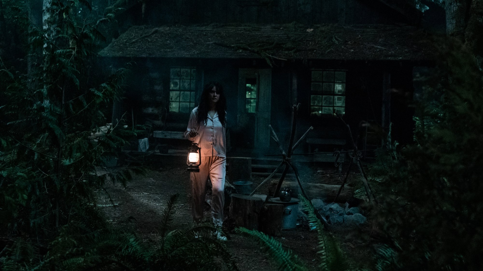 Une fille en pyjama à l'extérieur d'une cabane dans les bois tient une lanterne la nuit.