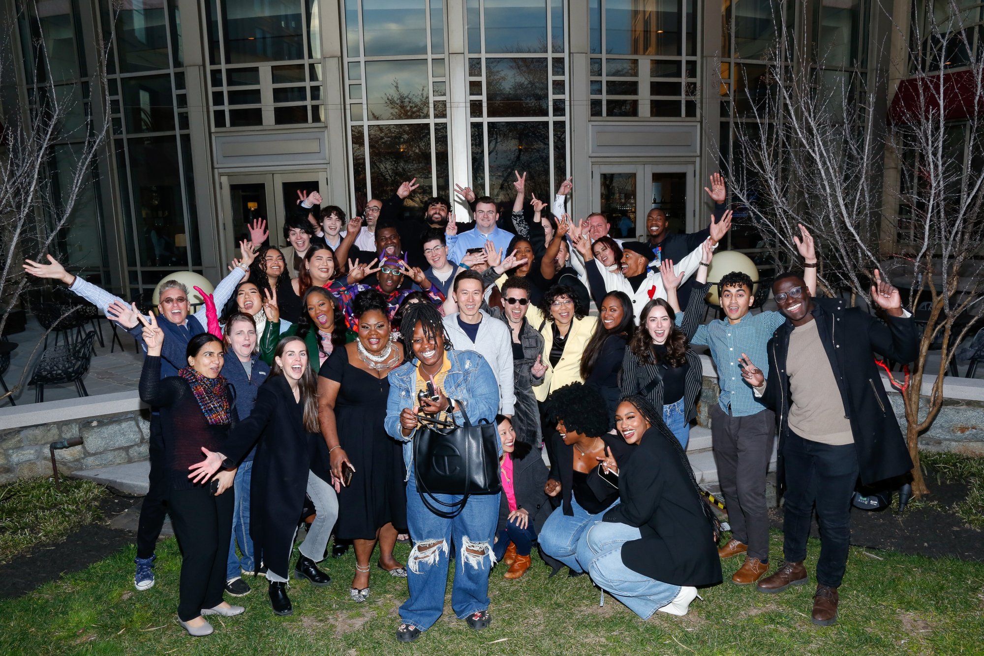 Un grand groupe de créateurs se tient à l'extérieur d'un centre de conférence et pose pour une photo flash. 