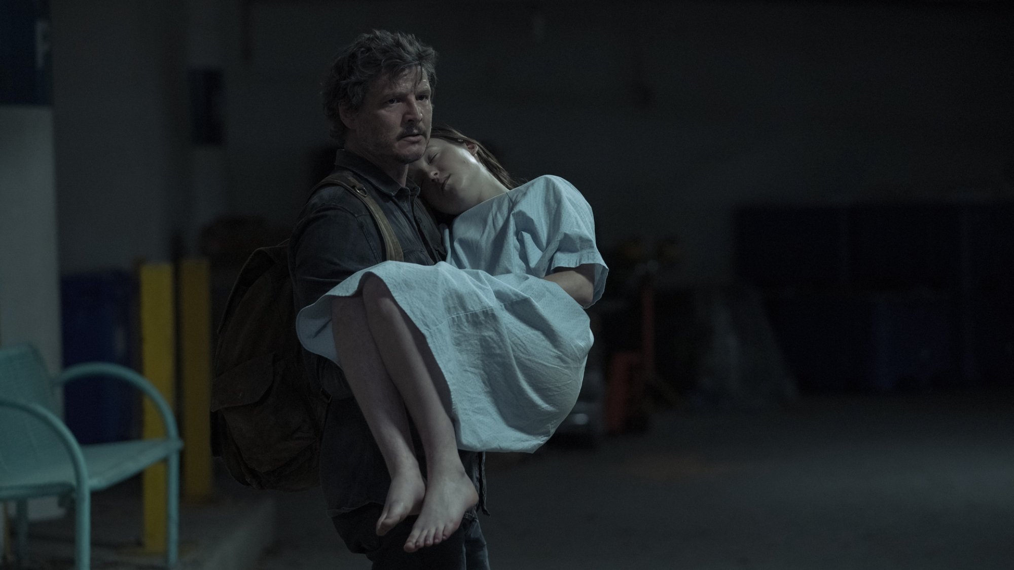 Un homme tient un adolescent dans ses bras, qui dort et porte une chemise d'hôpital.