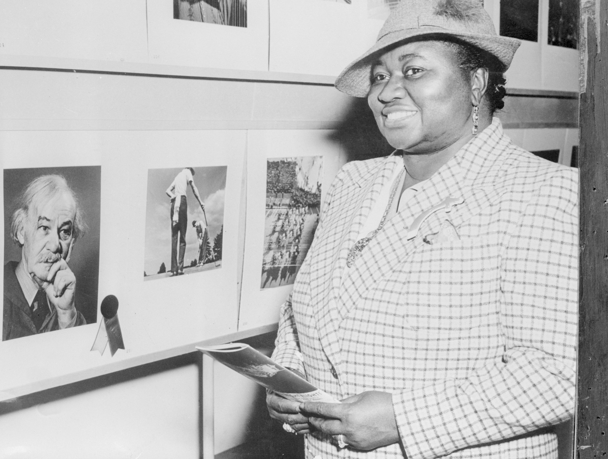 Une photo en noir et blanc de Hattie McDaniel posant devant une exposition de photos.
