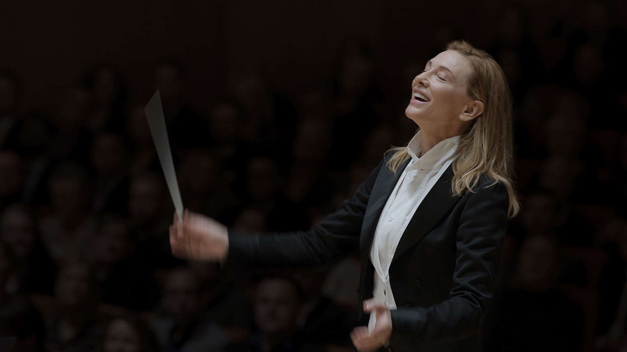 Une femme dirige un orchestre les yeux fermés en souriant.