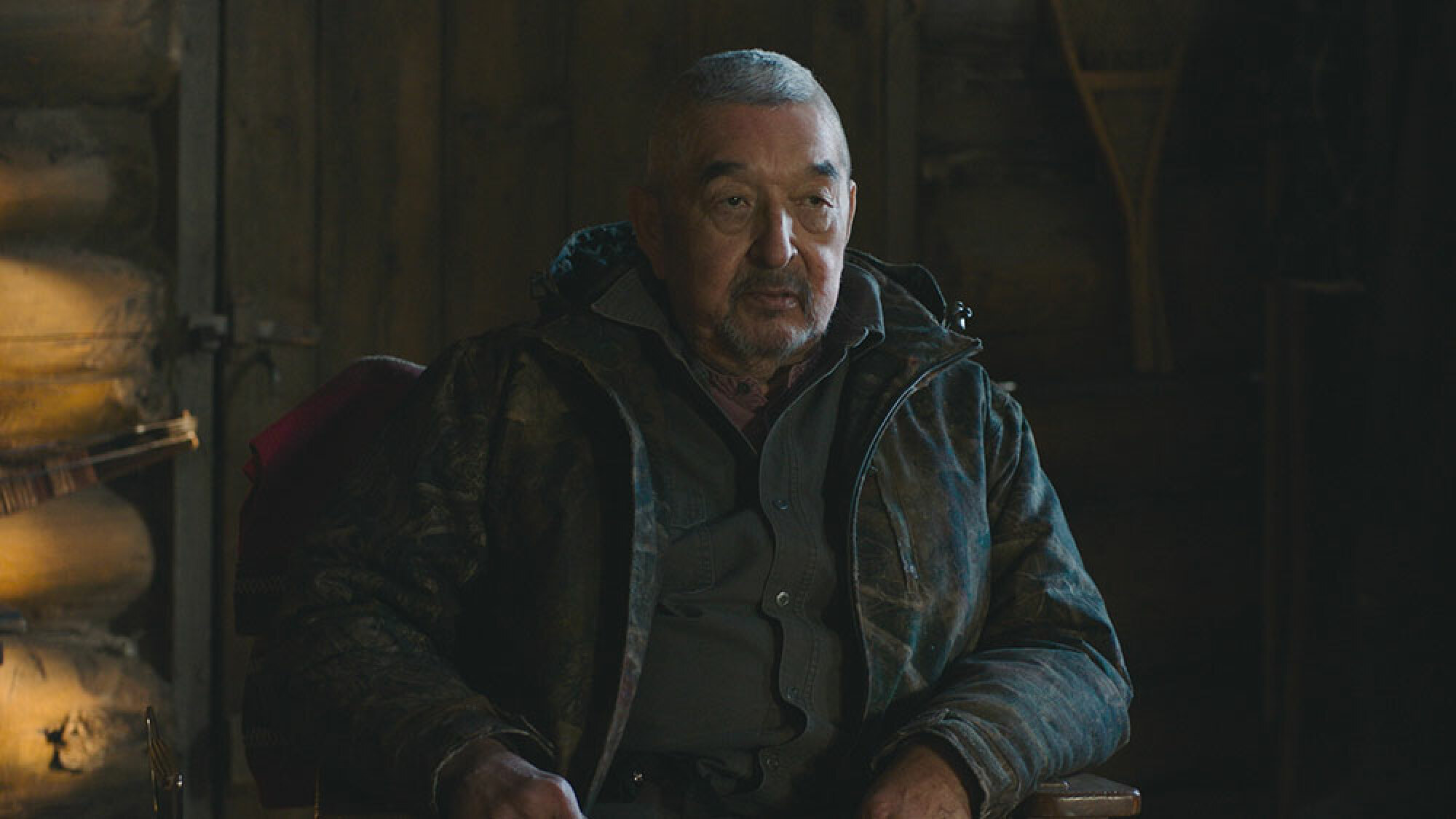 Un homme plus âgé est assis dans une cabane en bois.