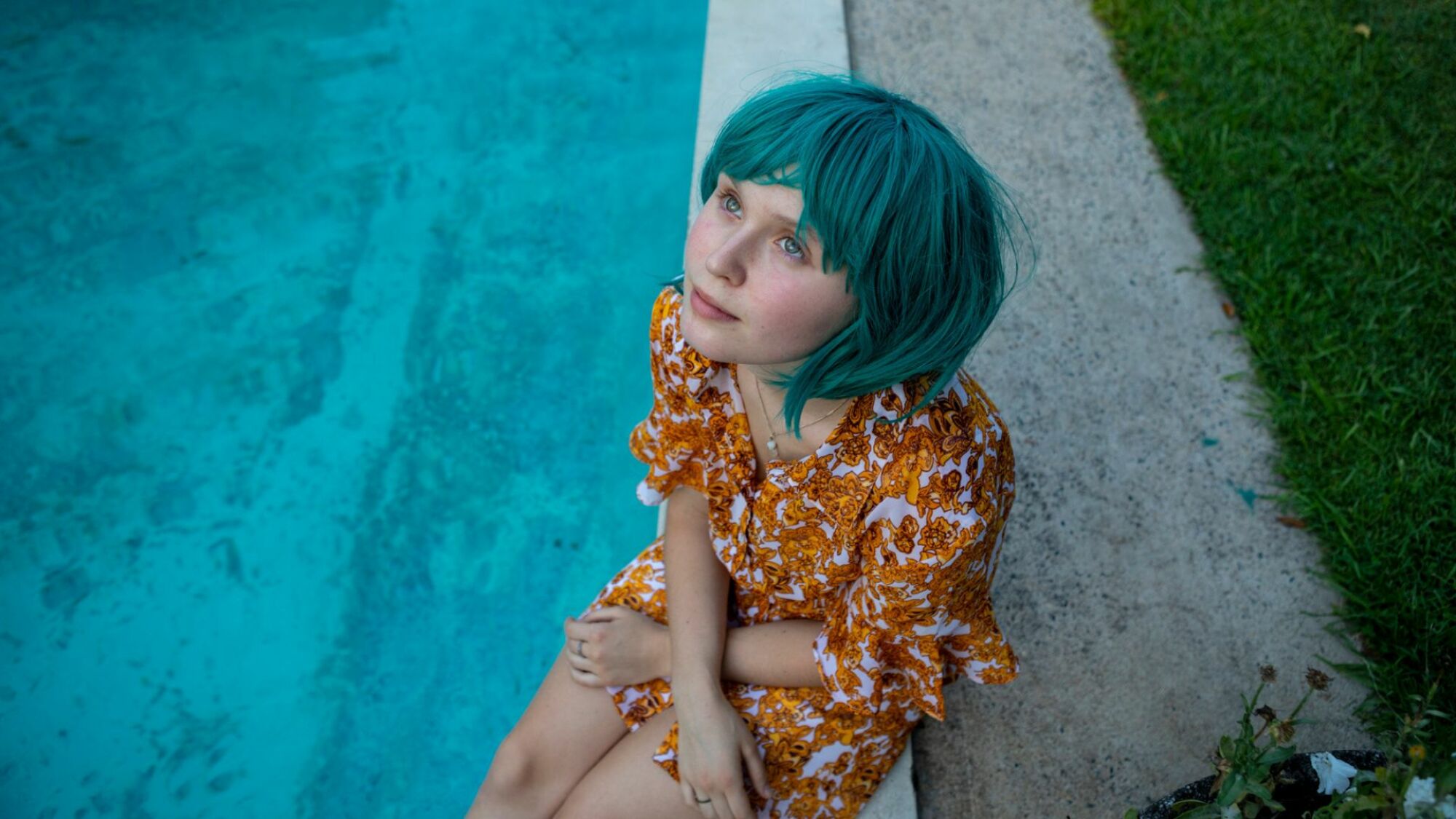 Une fille avec une perruque bleue est assise près d'une piscine.