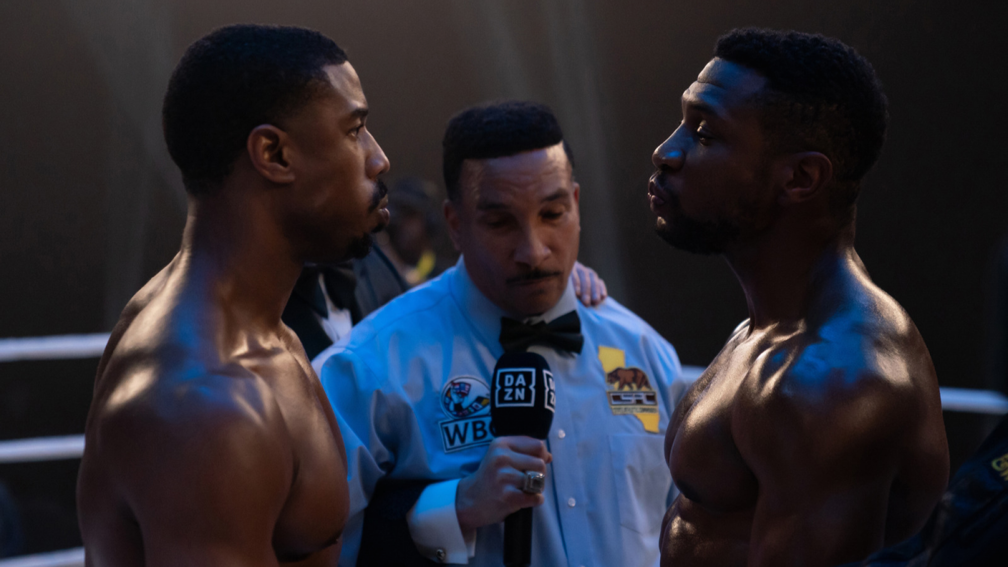 Deux hommes dans un ring de boxe se regardent avec un arbitre entre eux. 