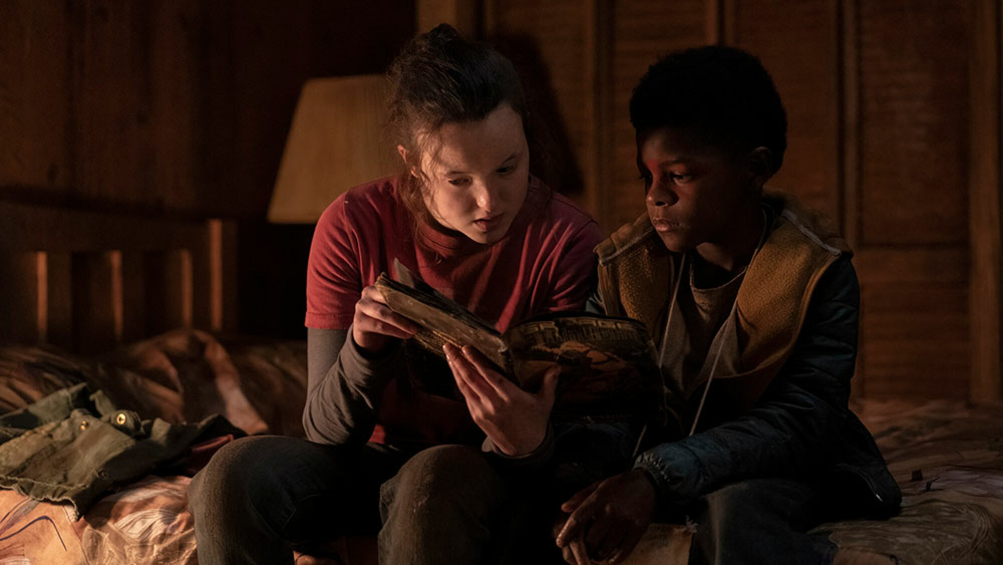 Une jeune fille et un garçon sont assis sur un lit en lisant une bande dessinée.