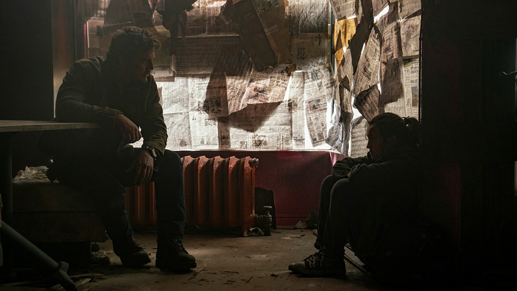 Un homme et une jeune fille discutent dans la pièce sombre d'un immeuble abandonné.  Les journaux couvrent les fenêtres.