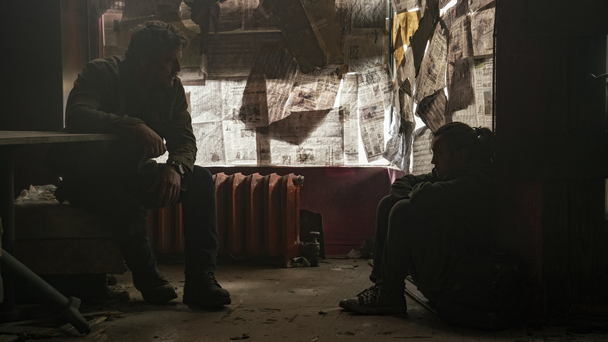 Un homme et un adolescent sont assis cachés dans une pièce dont les fenêtres sont recouvertes de papier journal.