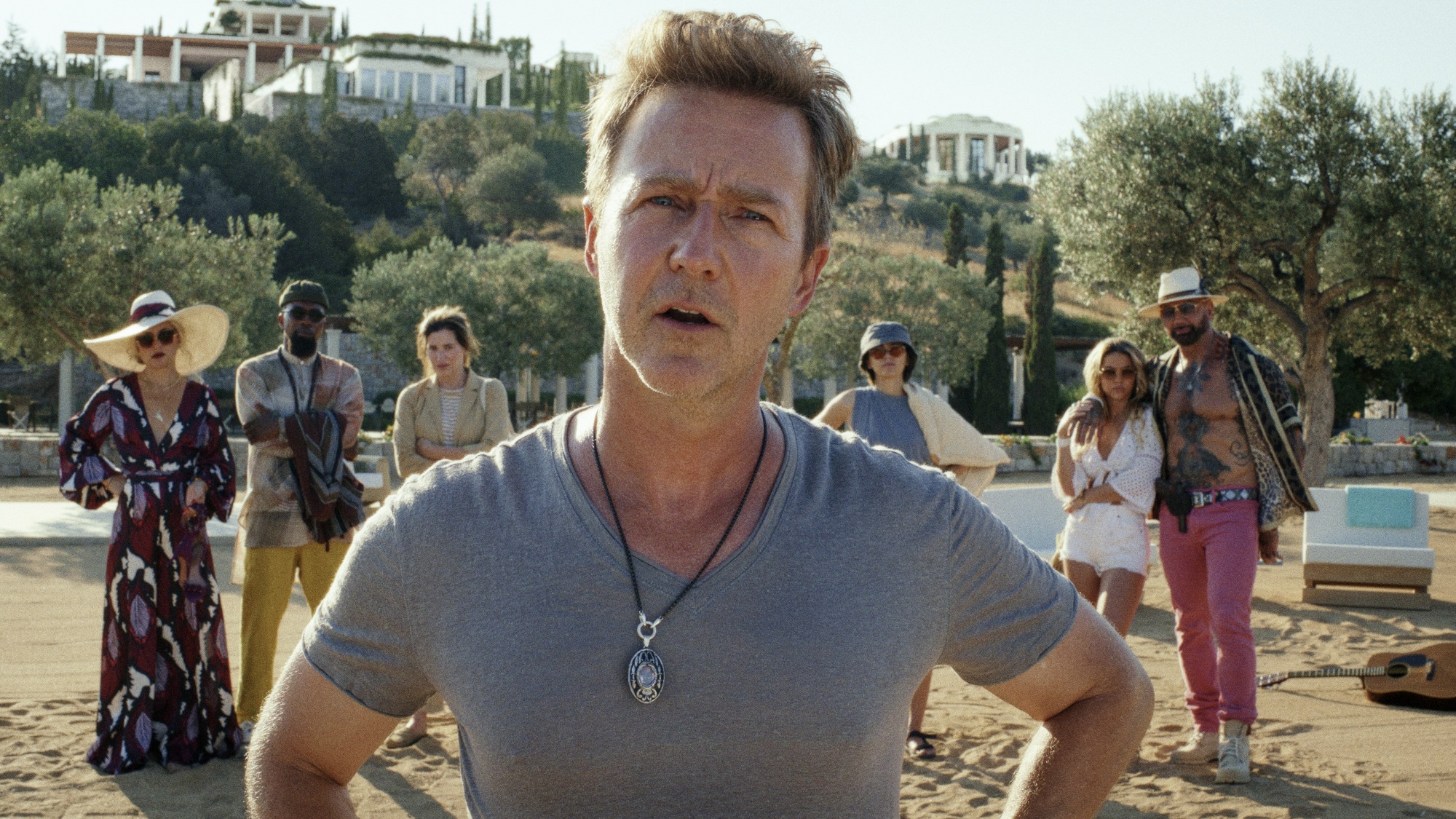 Un groupe de personnes se tient sur une plage, avec un homme devant qui pose ses mains sur ses hanches.