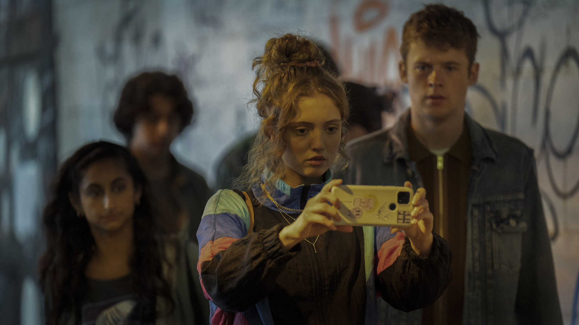 Un groupe d'adolescents se rassemble autour d'une adolescente qui tient son téléphone en mode paysage.