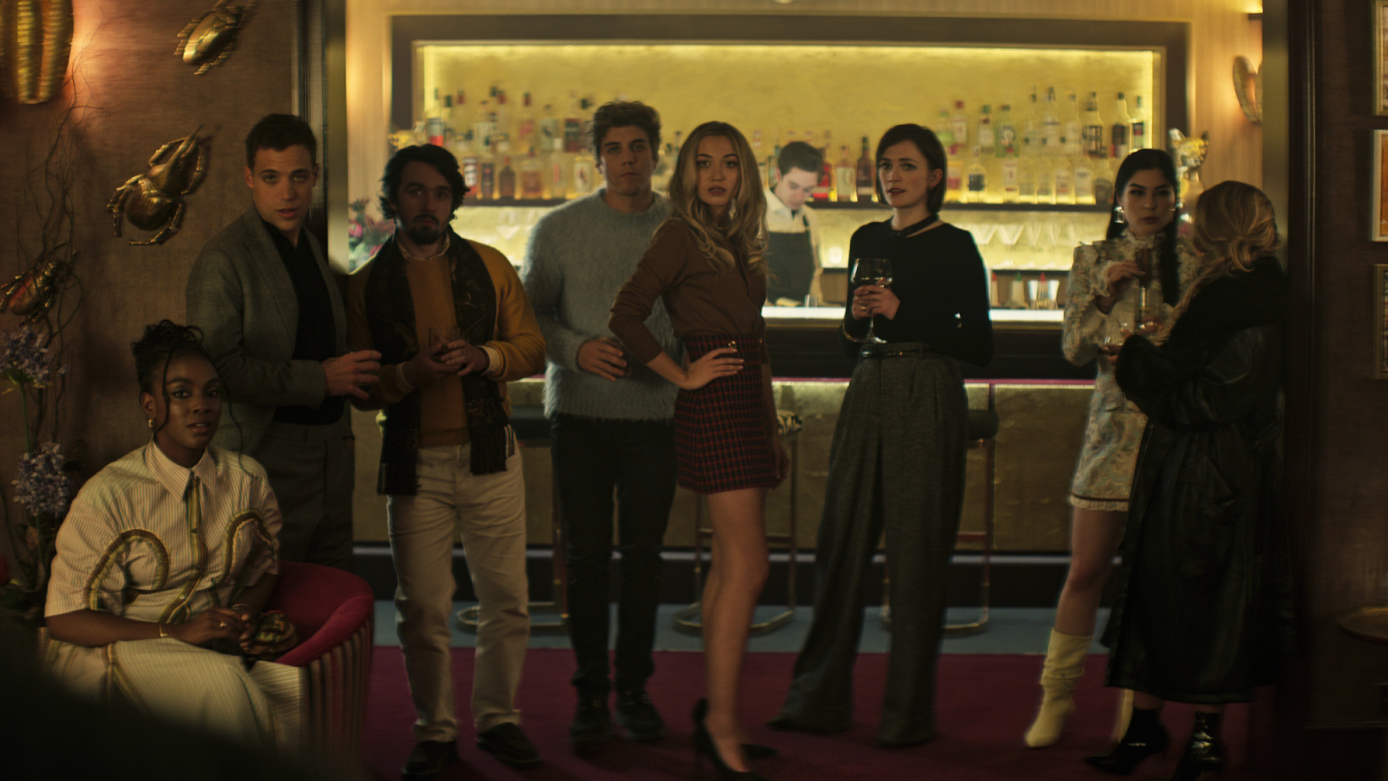 Un groupe d'amis en tenue de cocktail se tient devant un bar. 