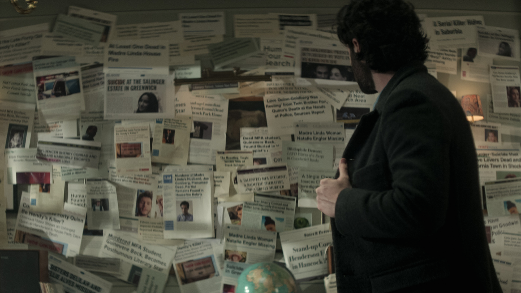 Un homme regarde un tableau désordonné de coupures de journaux. 
