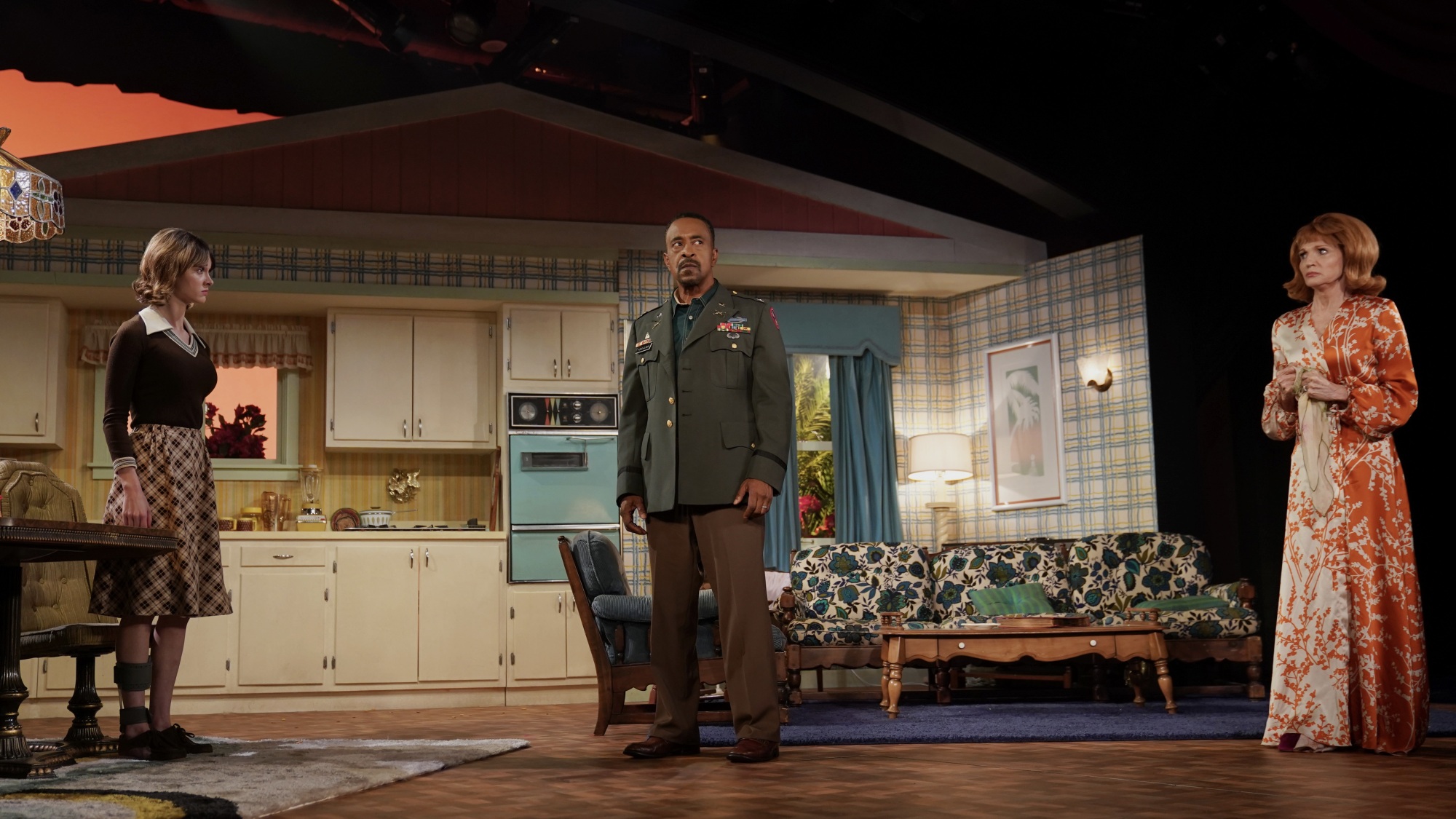 Trois acteurs se tiennent sur scène dans un décor conçu pour ressembler à une maison du milieu du siècle en Floride.