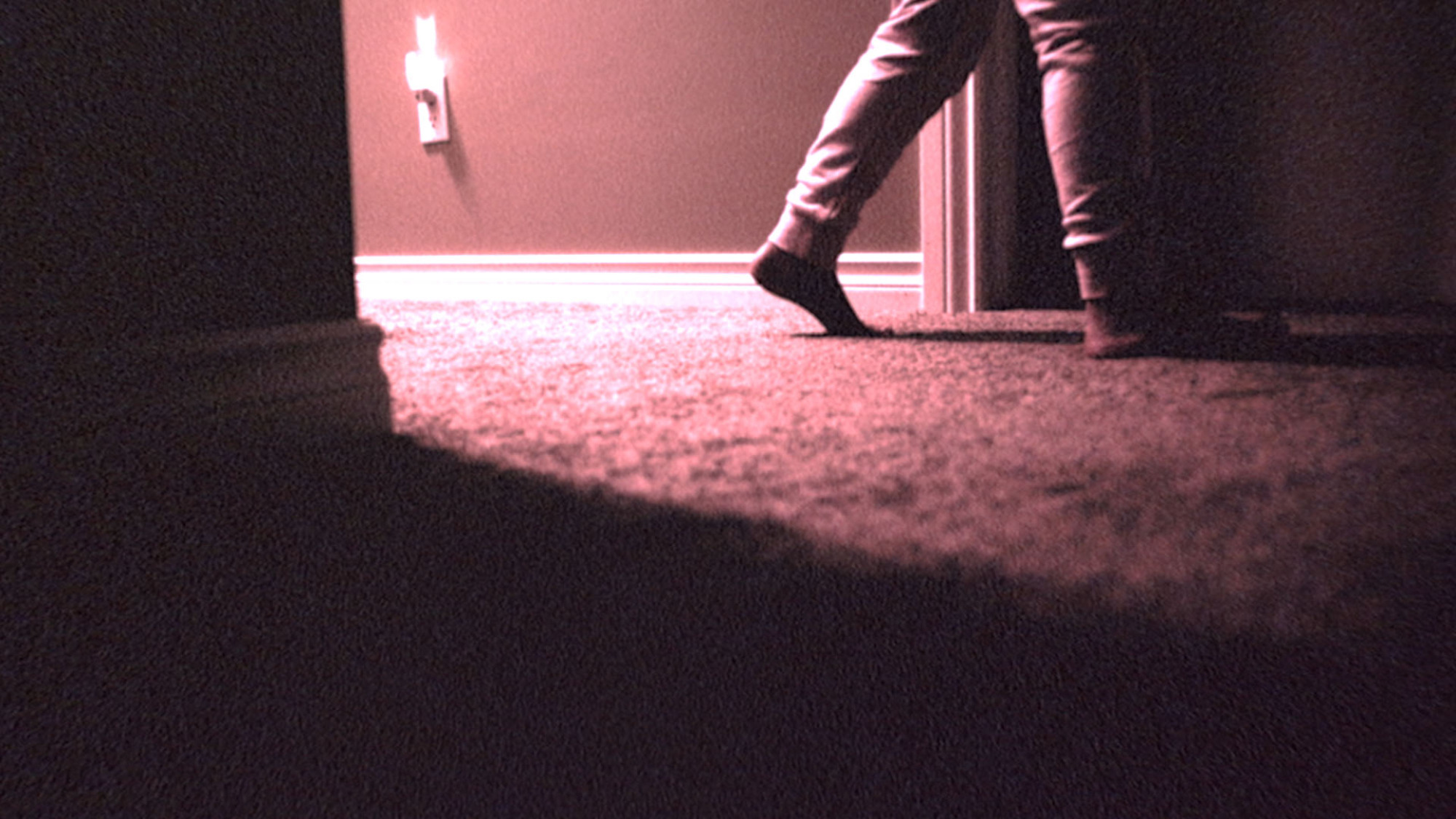 Une paire de pieds d'enfants sur un tapis, éclairée par une veilleuse, s'arrête près d'une porte.
