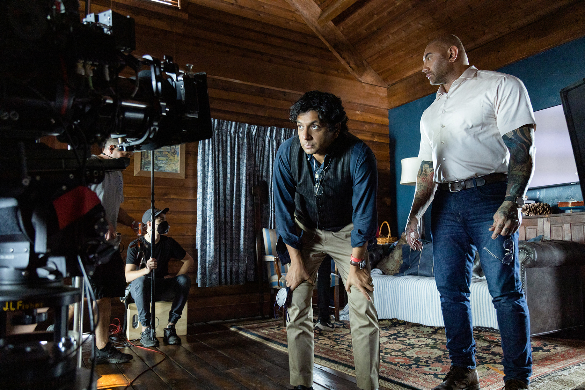 Un réalisateur s'appuie sur ses jambes en regardant dans une caméra à côté d'un acteur sur un plateau de tournage qui ressemble à un intérieur de cabine.