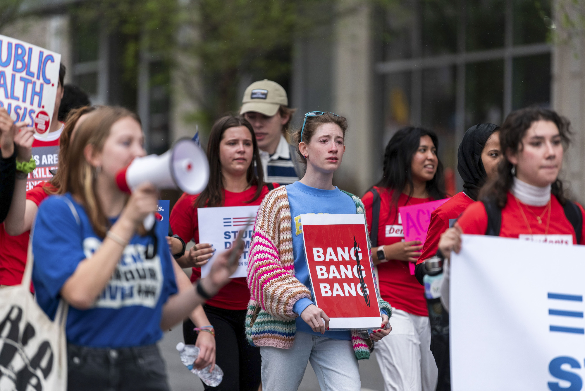 Un groupe d'étudiants émotifs marche avec des pancartes rouges et blanches et tient des mégaphones. 