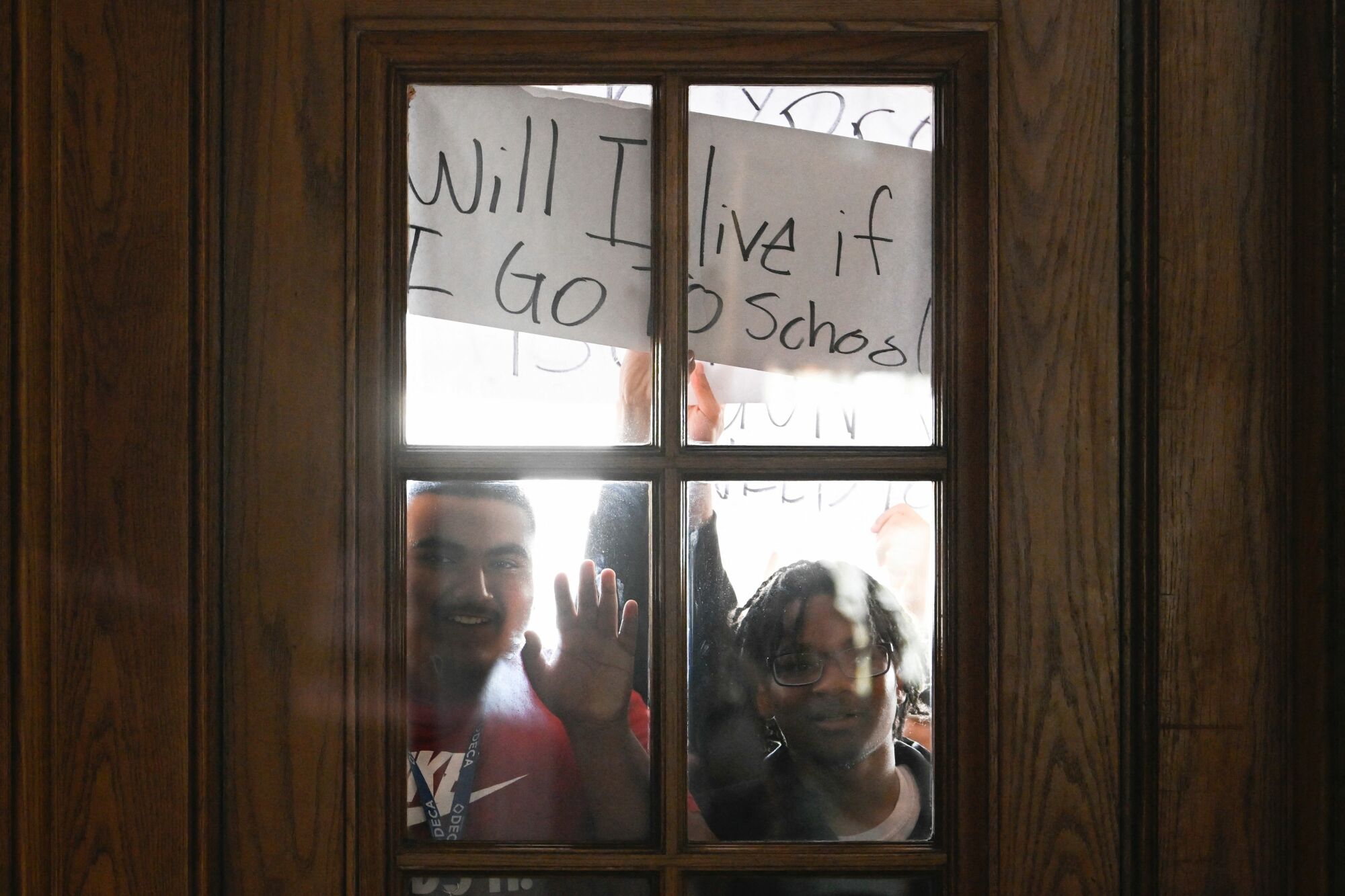 Les élèves regardent à travers une fenêtre tenant une pancarte qui dit, 