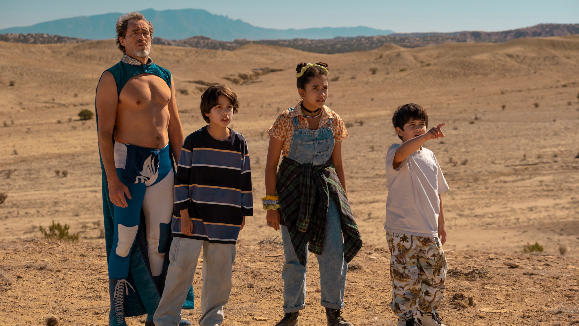 Trois enfants et un homme se tiennent dans le désert au Mexique, l'homme portant une cape de luchador.