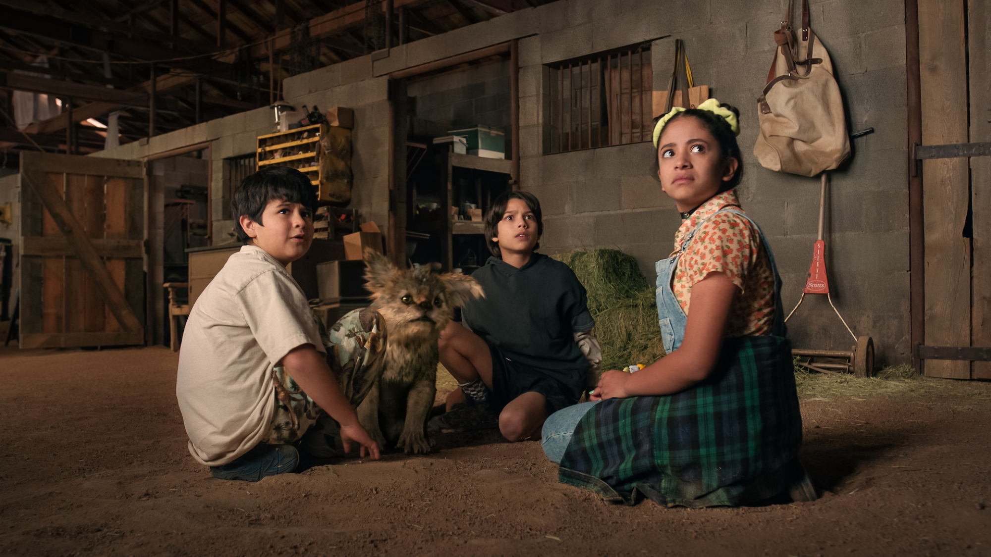 Trois enfants sont assis autour d'une petite bête mythique dans une grange.