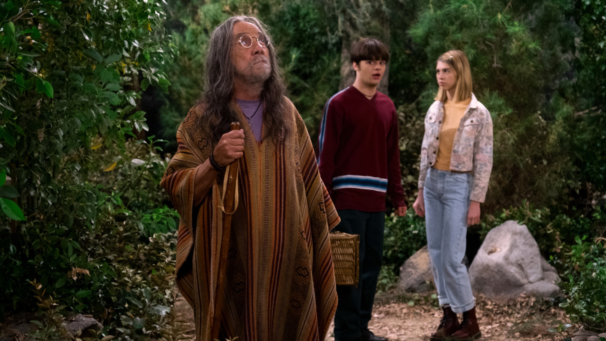 Hippie se tient dans une forêt avec deux adolescents confus qui le regardent. 