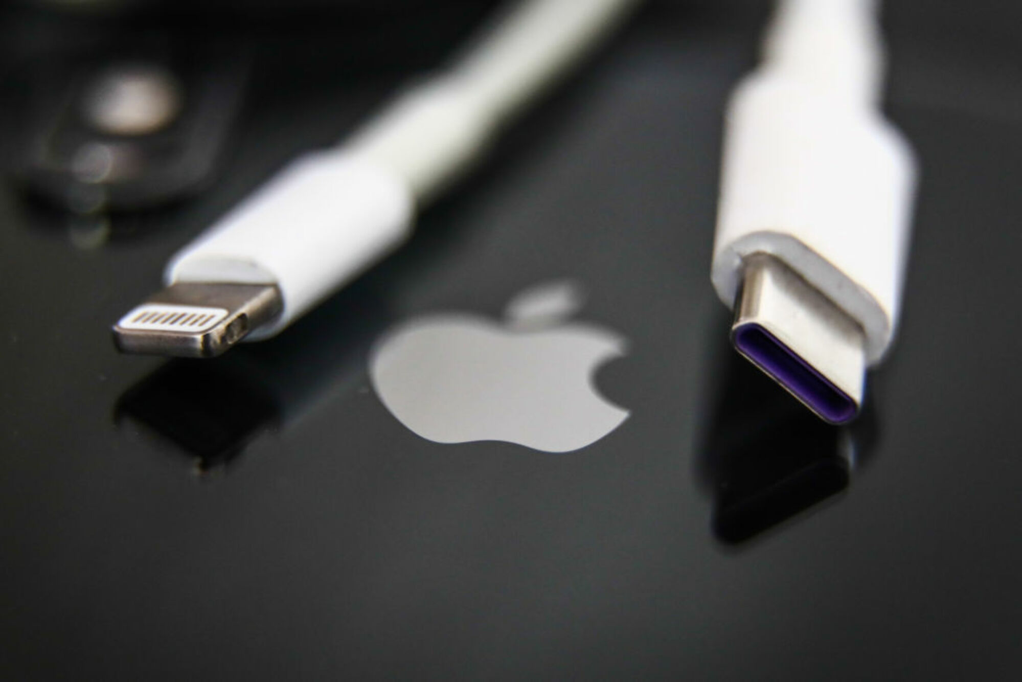 un câble Lightning et un câble USB-C au-dessus d'un iPhone affichant le logo Apple