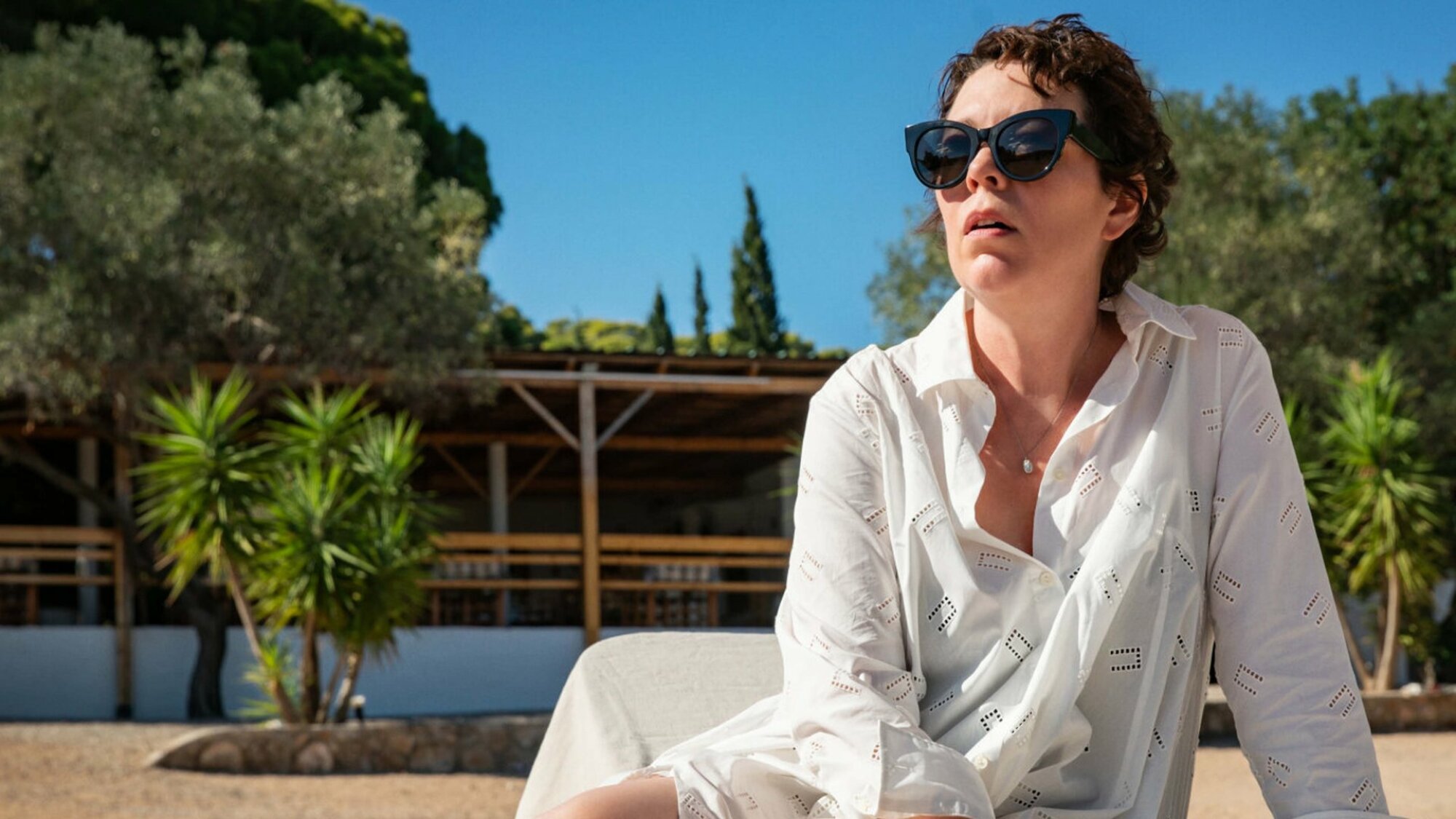 Une femme est assise sur une chaise de plage portant une chemise blanche et des lunettes de soleil.