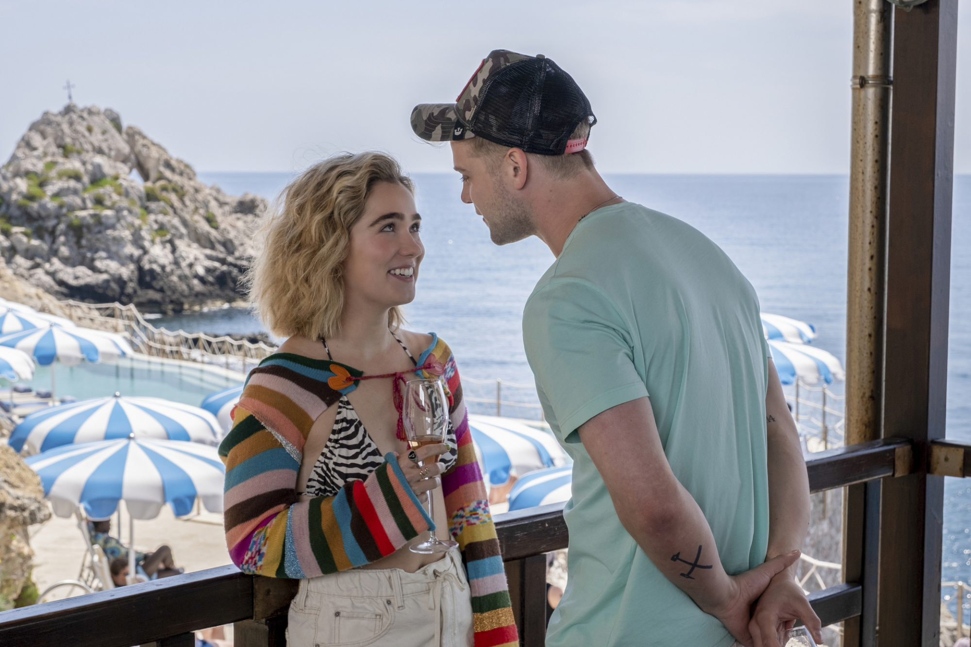 Jack se penche sur Portia lors d'une fête sur la plage.  Elle porte un gilet multicolore sur un haut de bikini imprimé zèbre. 