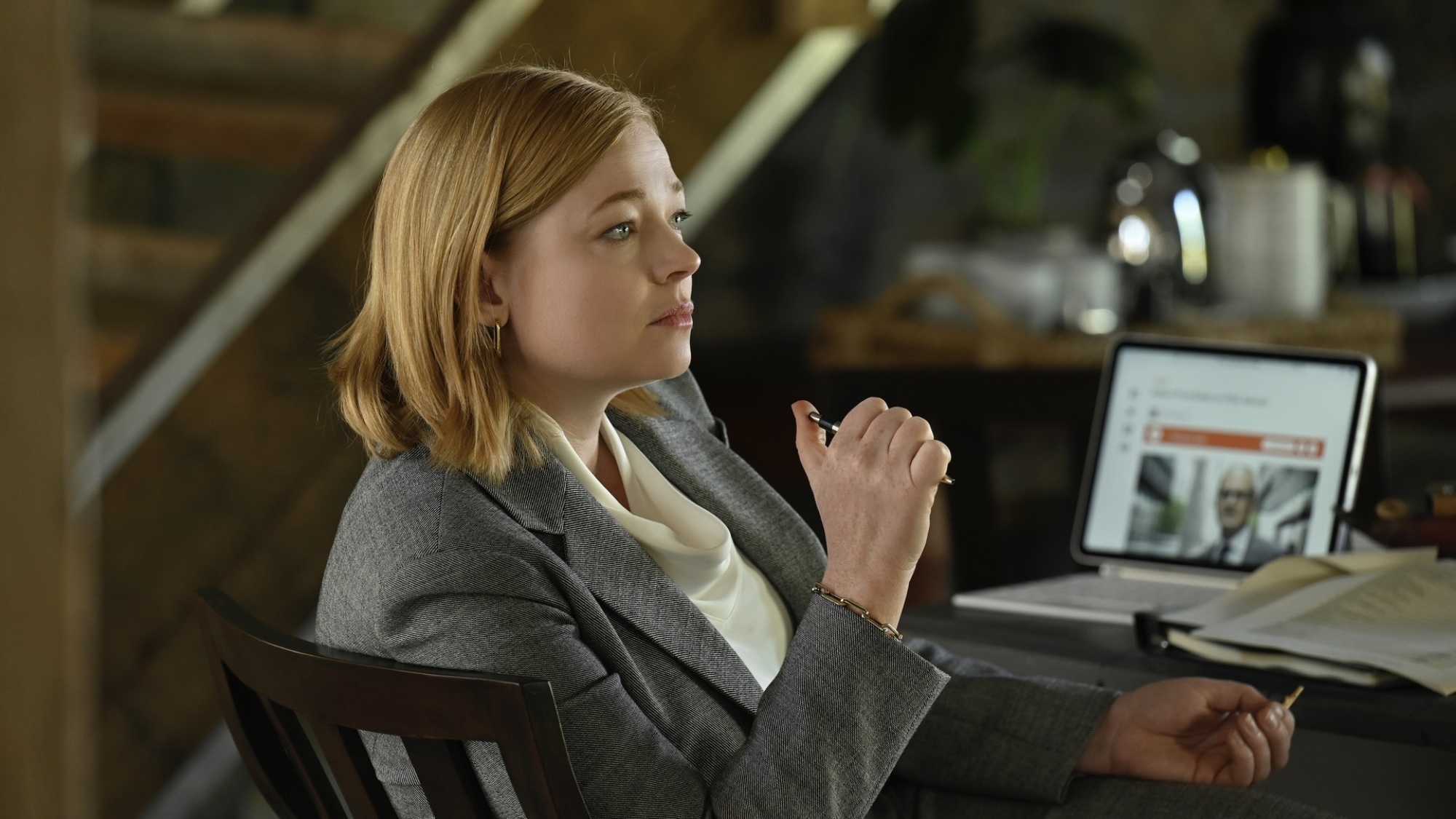 Une femme en costume gris est assise à une table avec un ordinateur portable dessus.