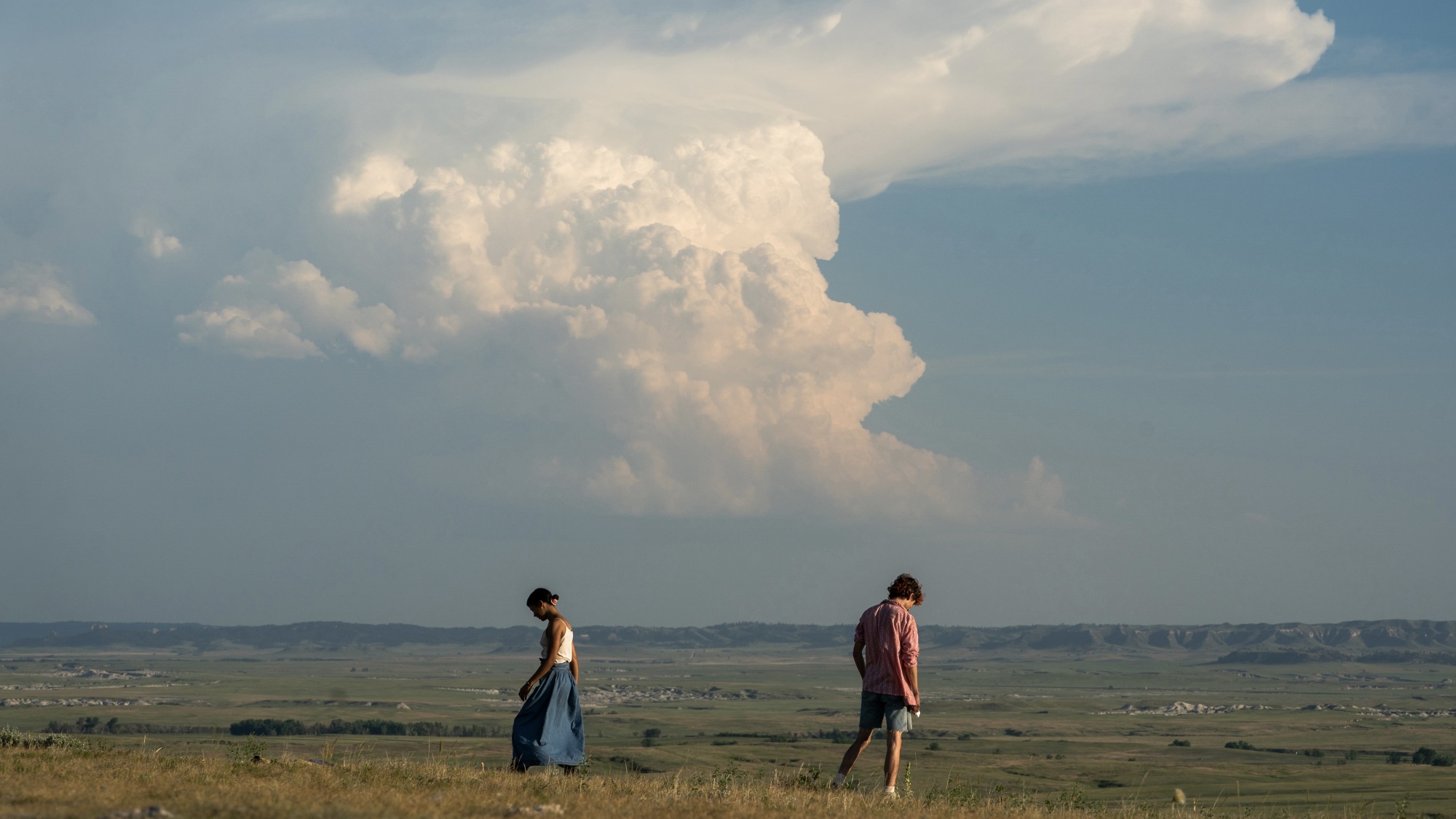 Un jeune homme et une femme debout dans un champ avec un gros nuage orageux qui se profile au loin.