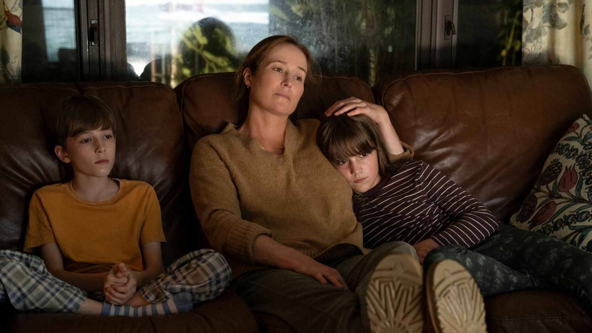 Une femme se repose sur un divan avec ses deux enfants. 