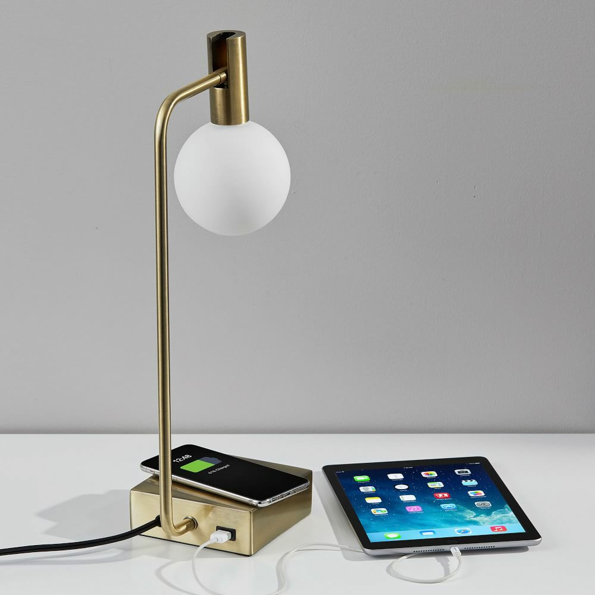 Lampe en laiton West Elm avec un smartphone en charge sur son socle et un ipad branché sur son port USB.