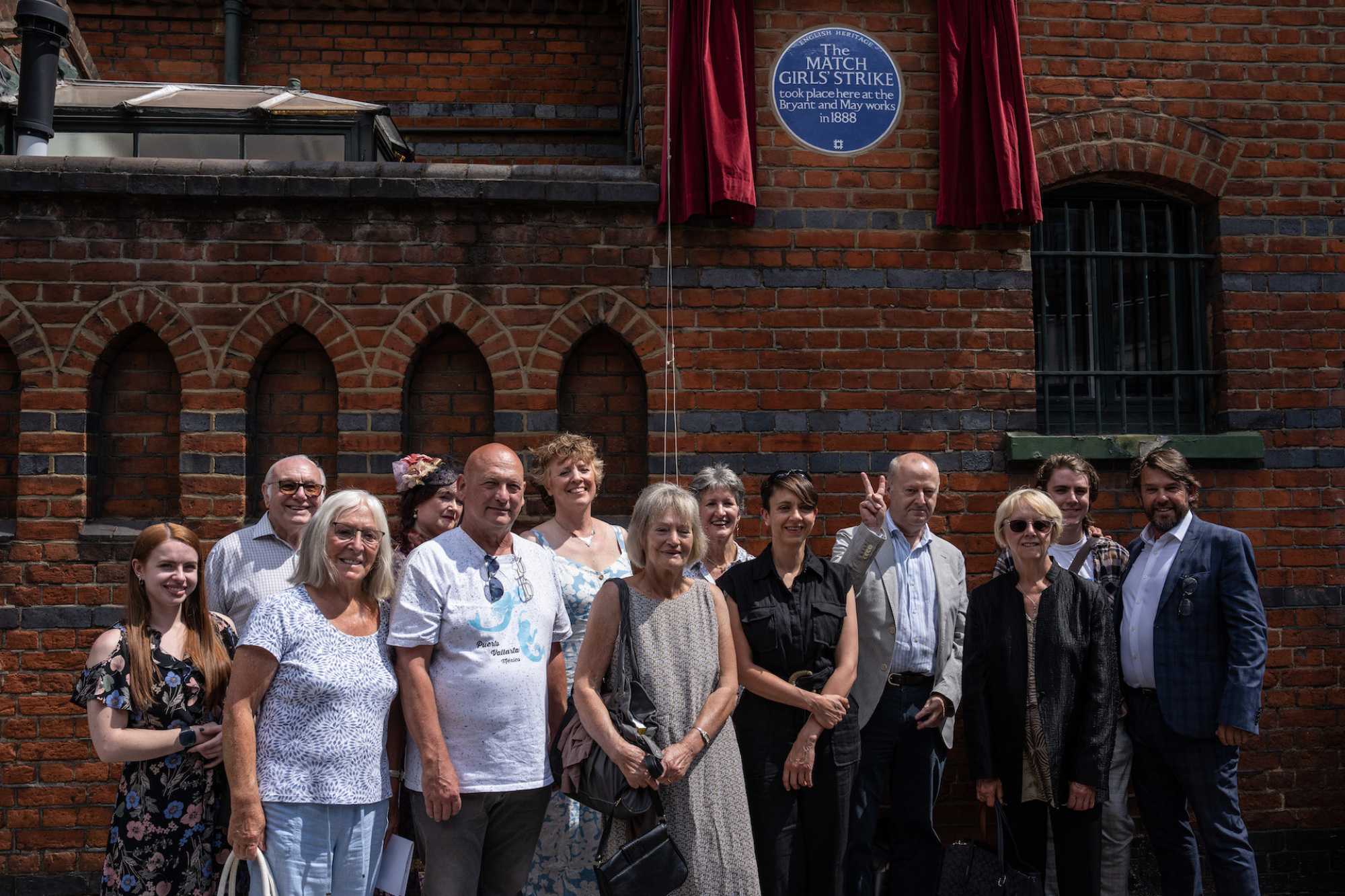 Un groupe de personnes se tient debout pour une photo ensemble devant un mur de briques avec une plaque bleue dessus.