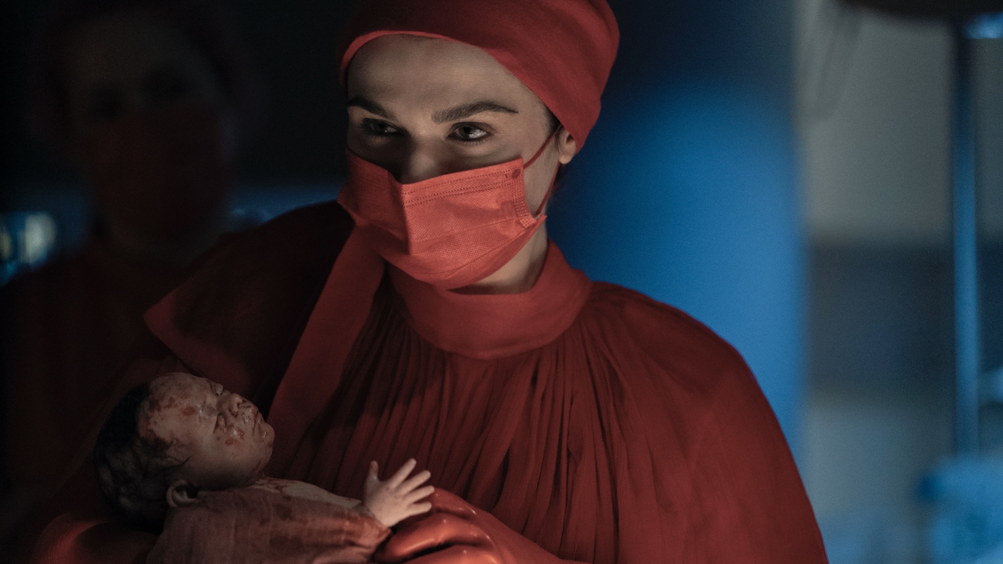 Une femme en blouse rouge et un masque d'hôpital rouge berce un nouveau-né ensanglanté.