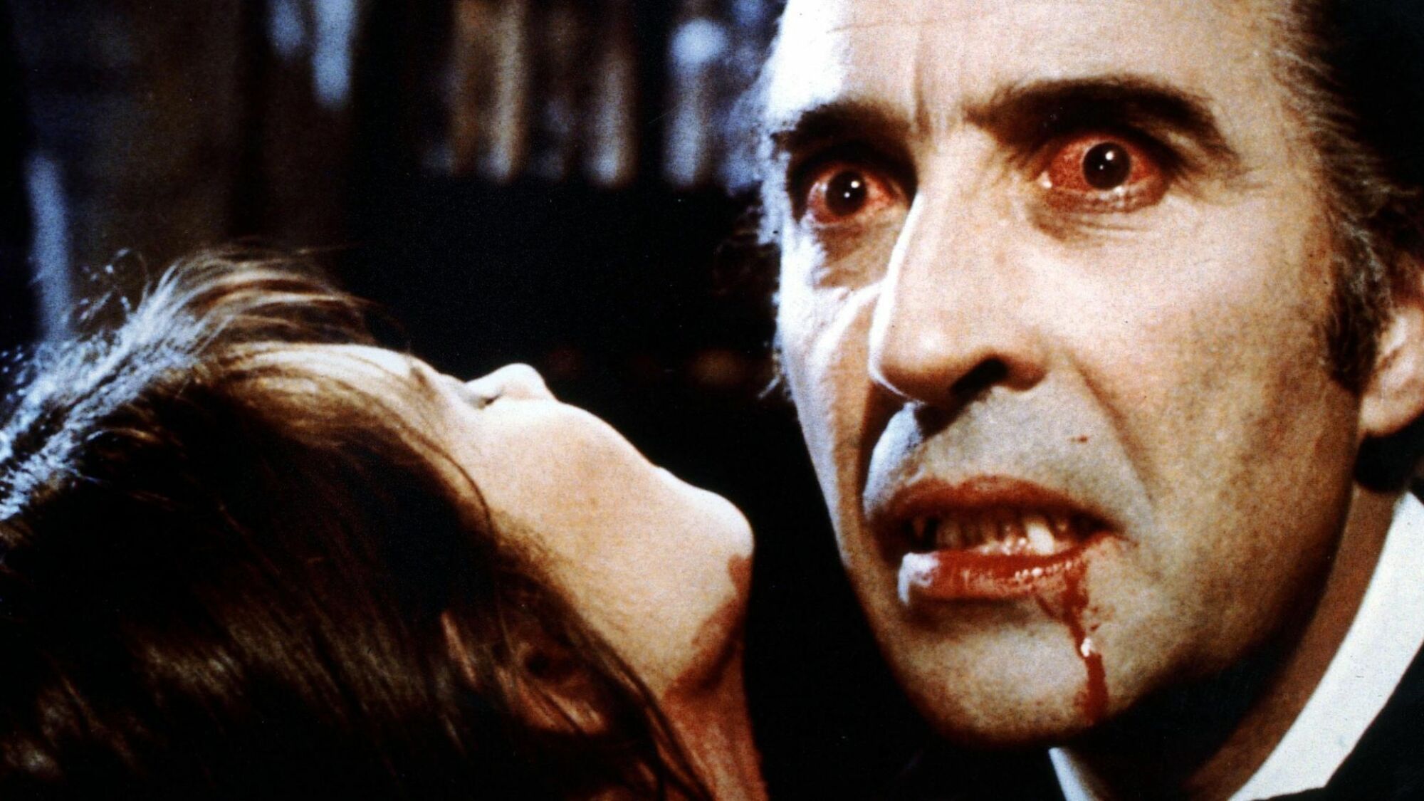 Christopher Lee joue Dracula avec du sang coulant sur son menton et une femme au premier plan. 