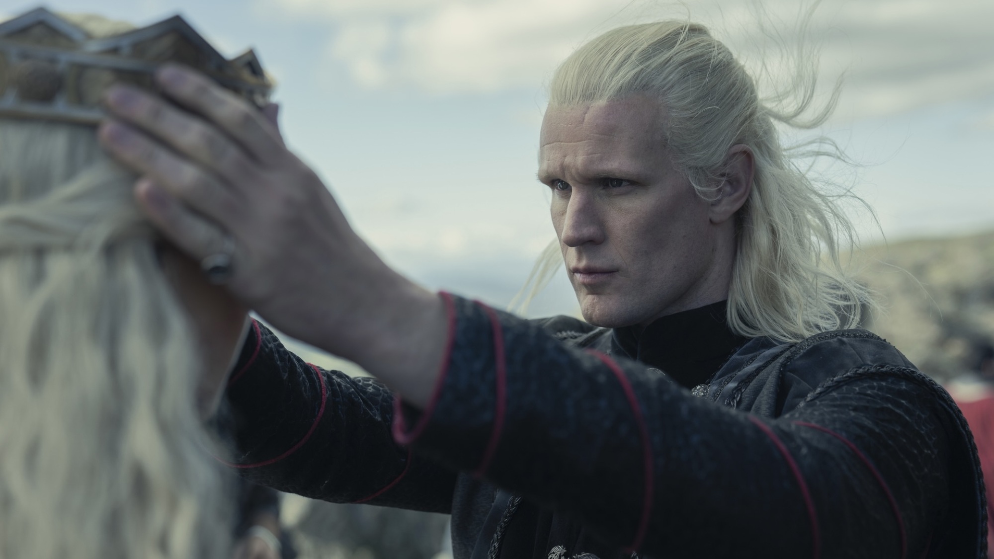 Un homme aux cheveux blonds argentés place une couronne en or sur la tête d'une femme aux cheveux blonds argentés.