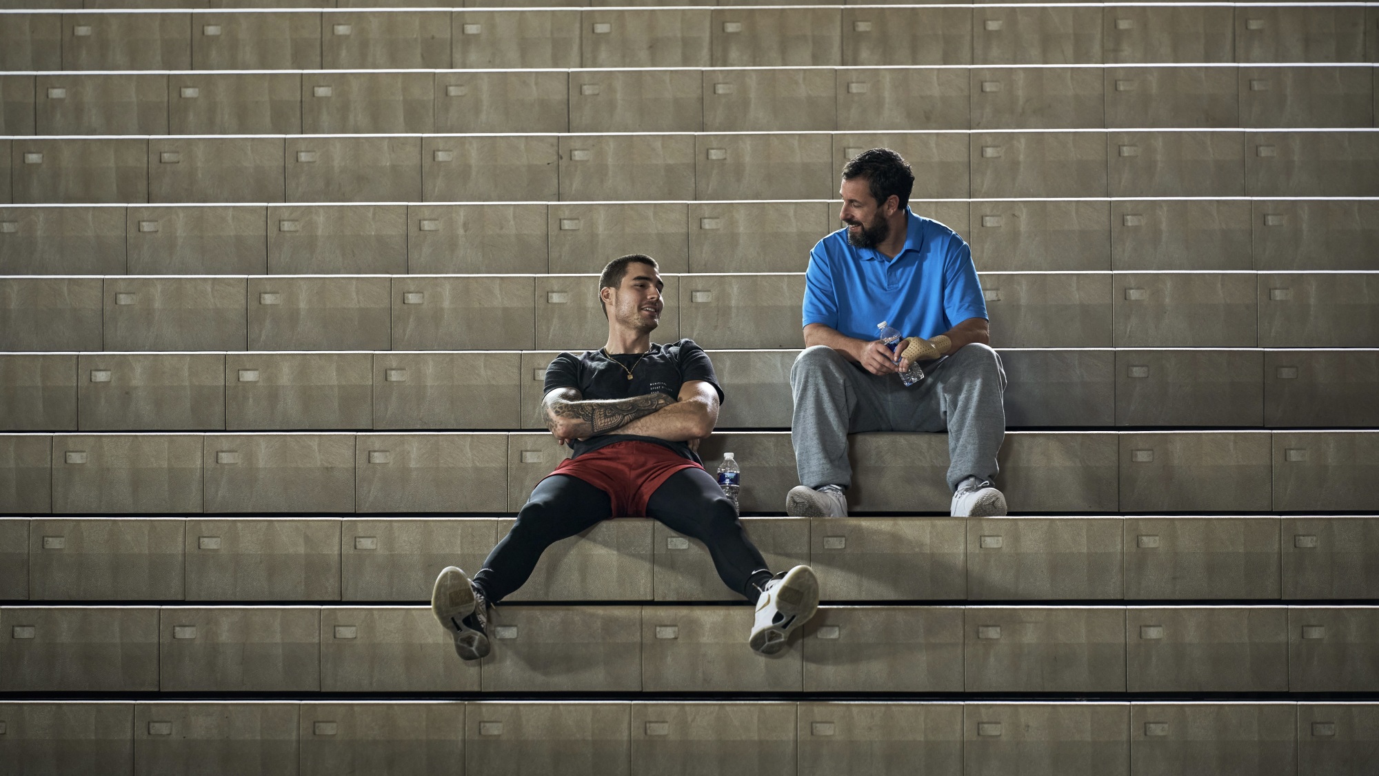 Deux hommes assis sur des gradins dans un gymnase de basket-ball.