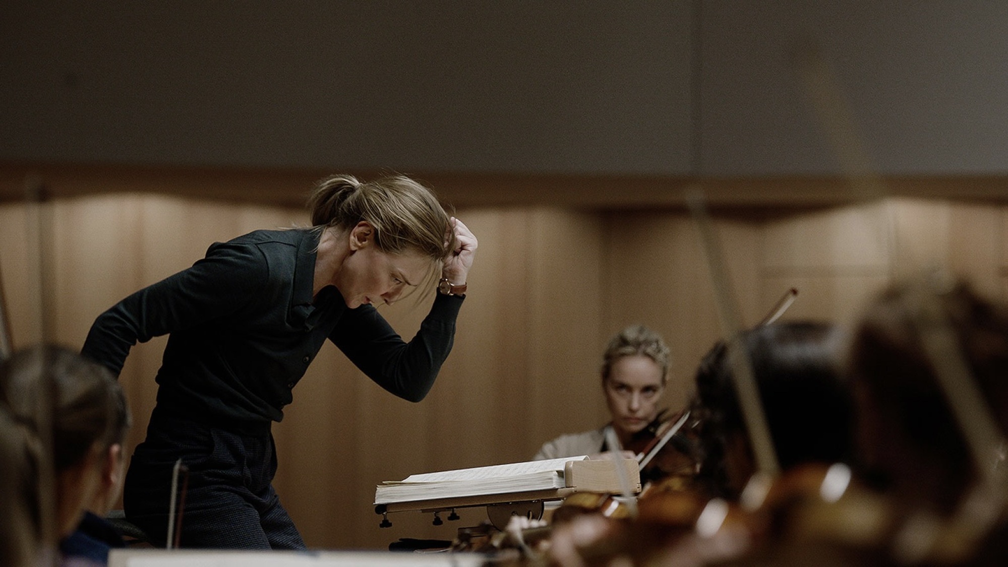 Un chef d'orchestre tout de noir vêtu lève le poing pour faire taire son orchestre.