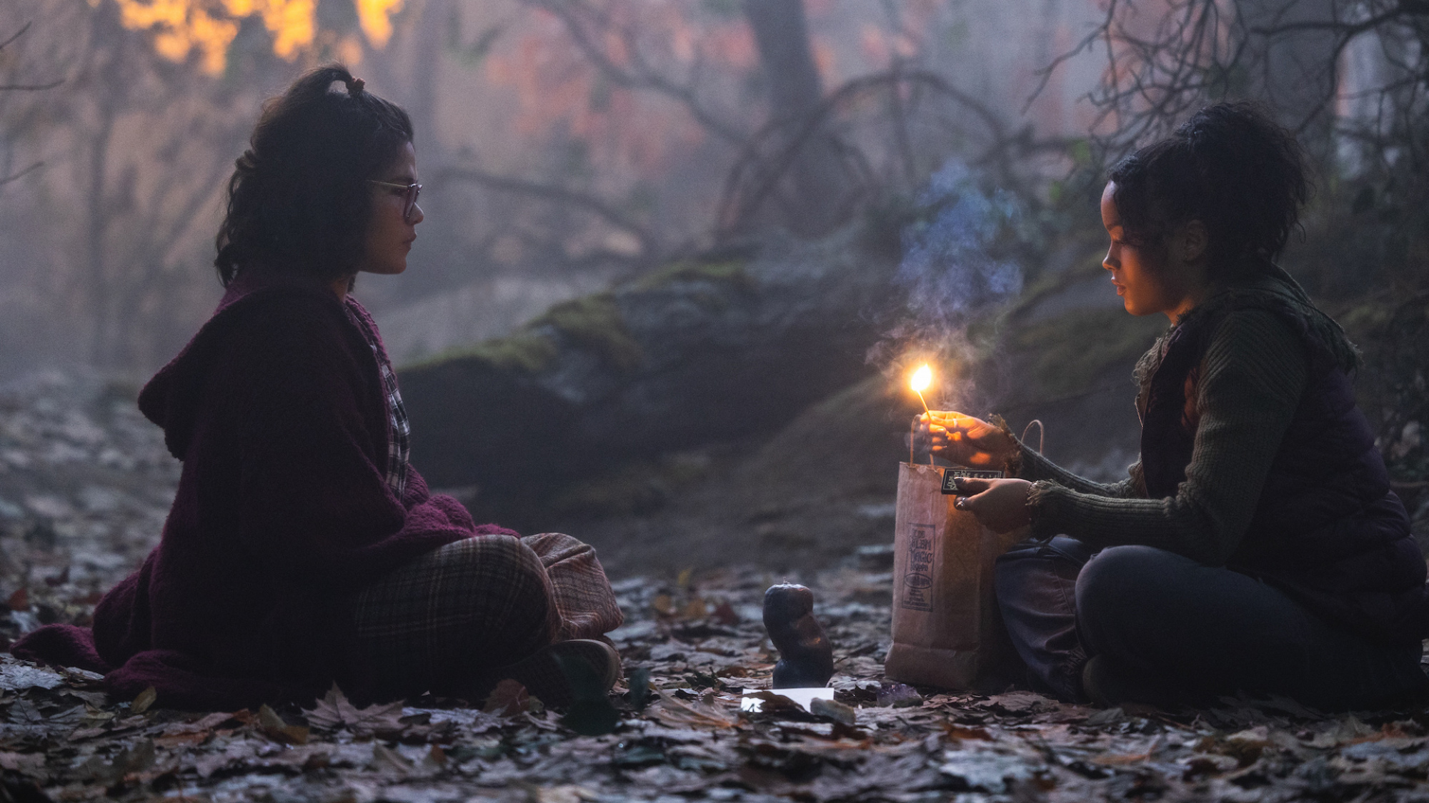 Deux filles sont assises dans un bois avec une bougie, face à face.