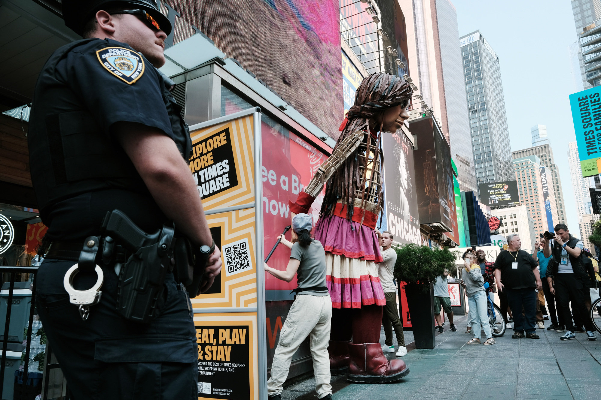 Amal s'appuie contre un immeuble.  Un policier de la ville de New York se tient au premier plan, les bras croisés devant lui.