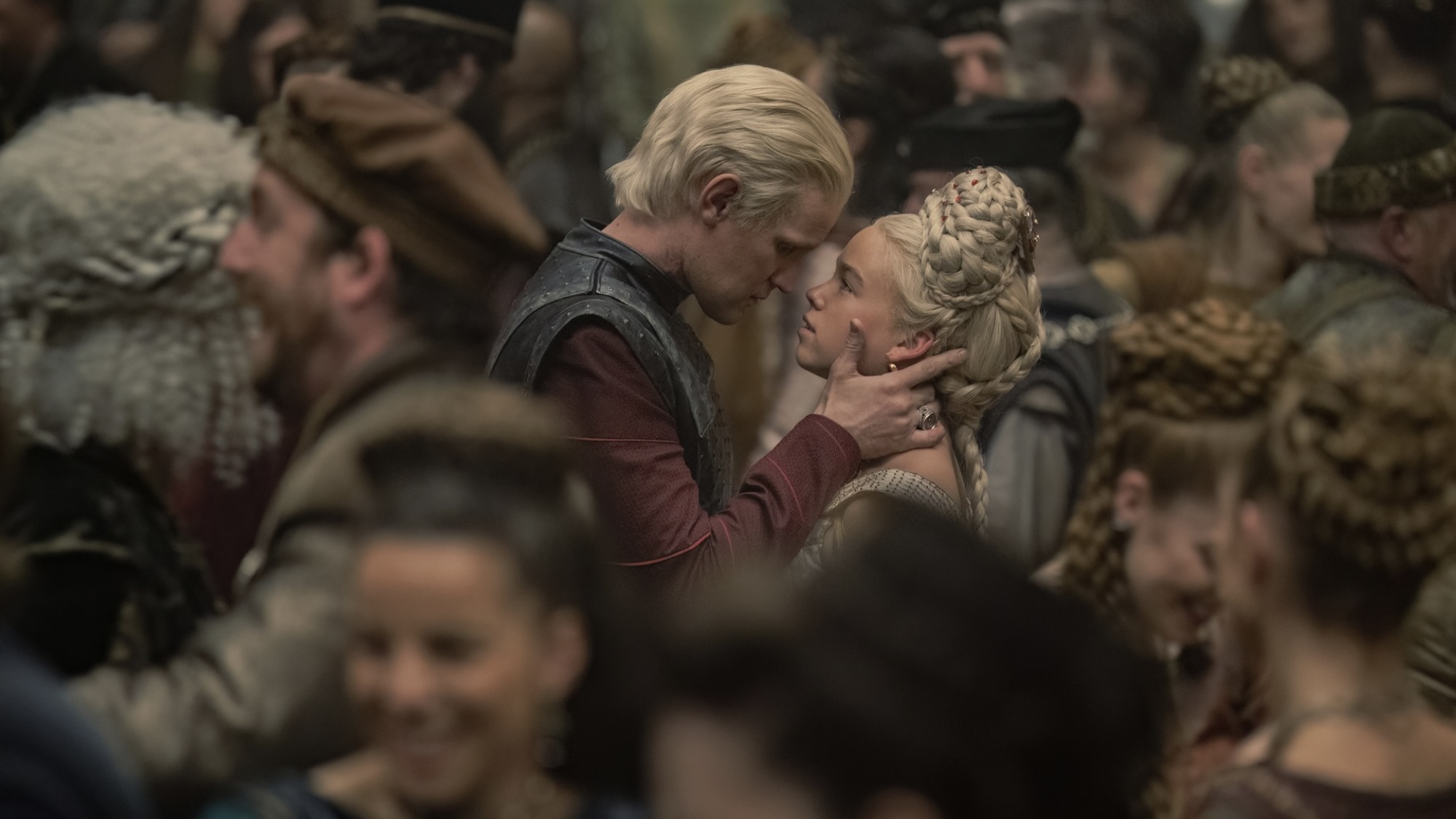 Un homme aux cheveux blonds argentés tient le visage d'une jeune femme aux cheveux blonds argentés.  Ils sont au milieu d'une piste de danse bondée.