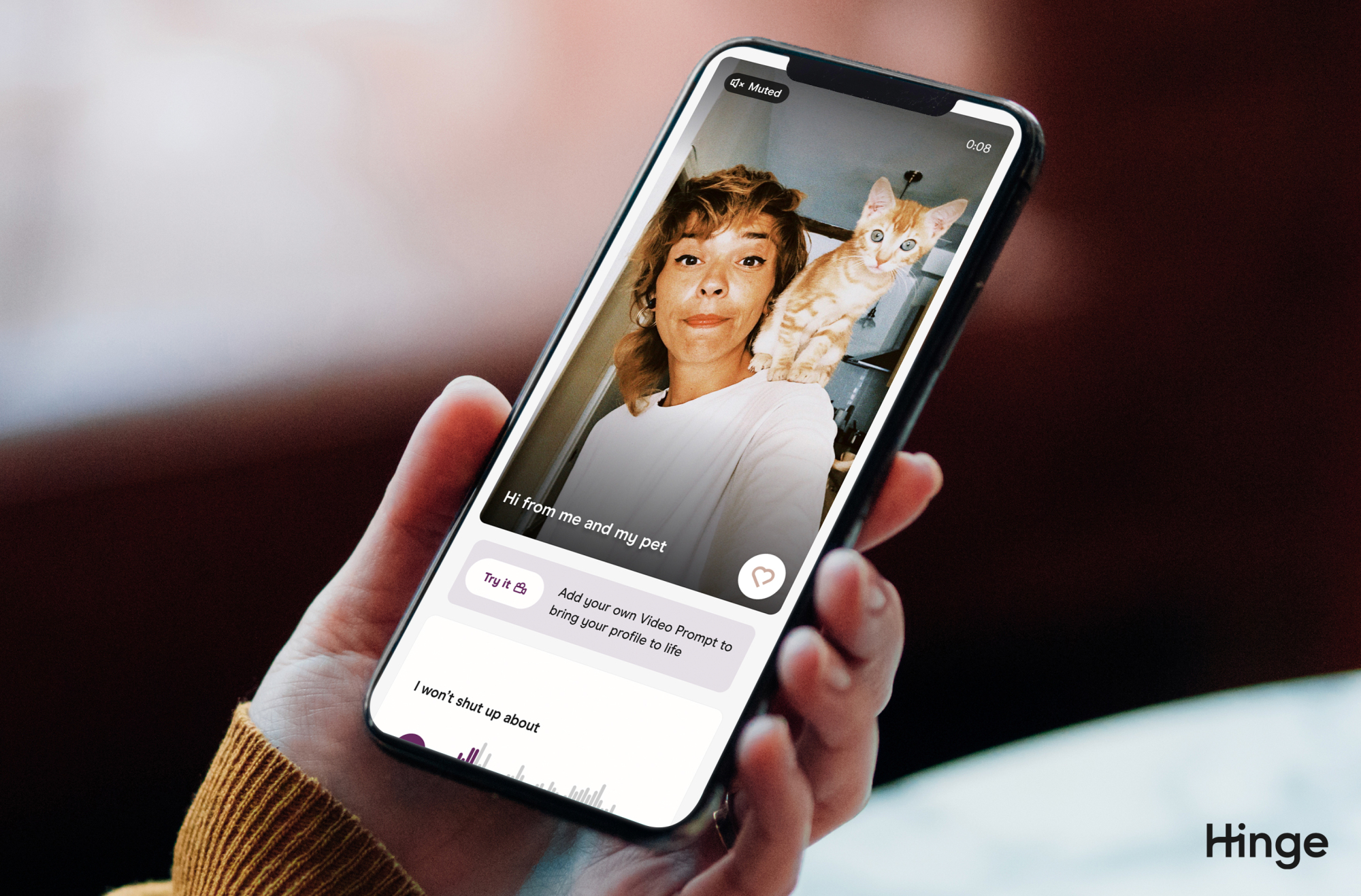 Une main tenant un téléphone avec l'application Hinge ouverte, un profil affiche la nouvelle fonctionnalité d'invite vidéo. 