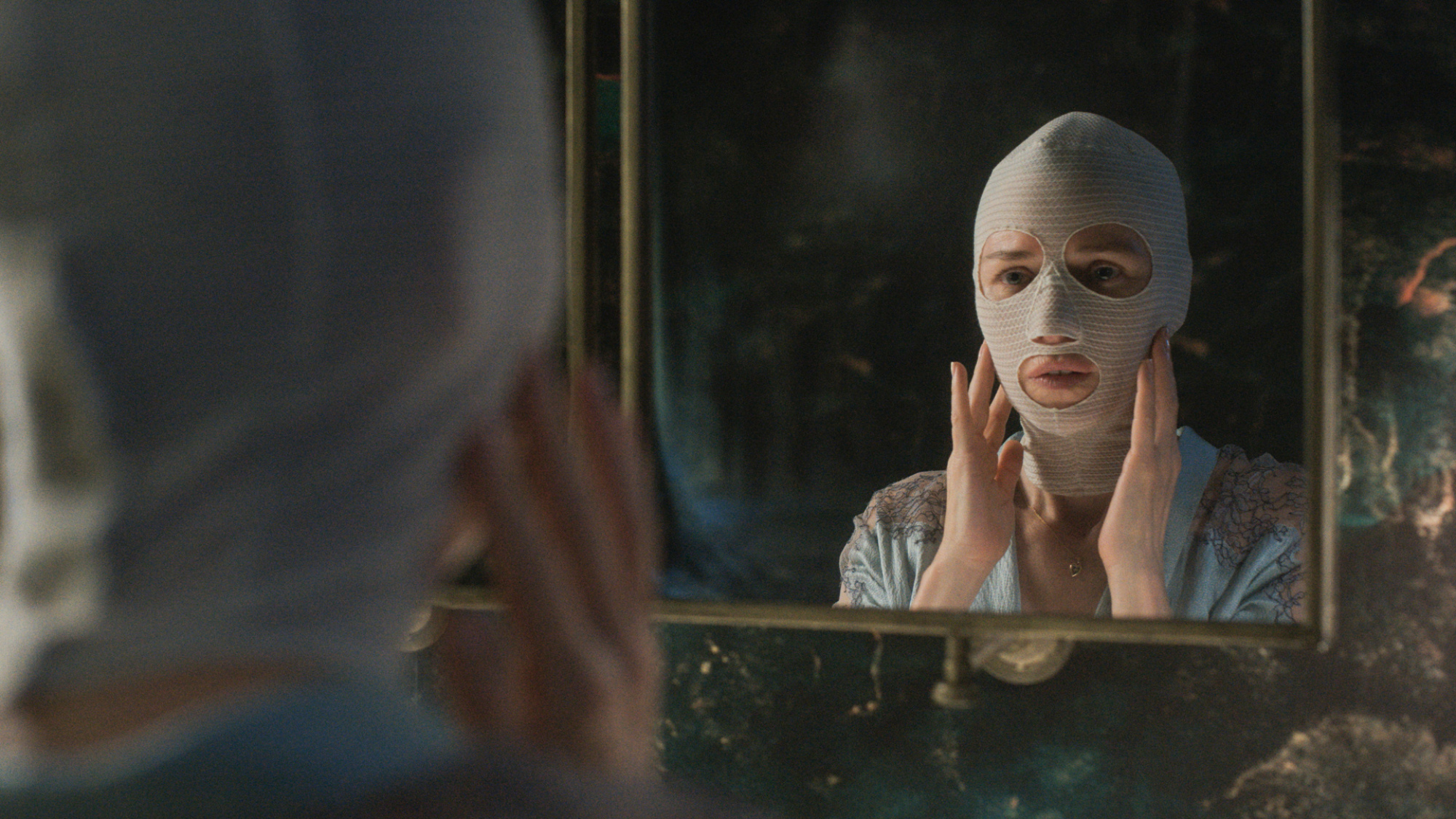 Une femme portant des bandages faciaux se regarde dans un miroir