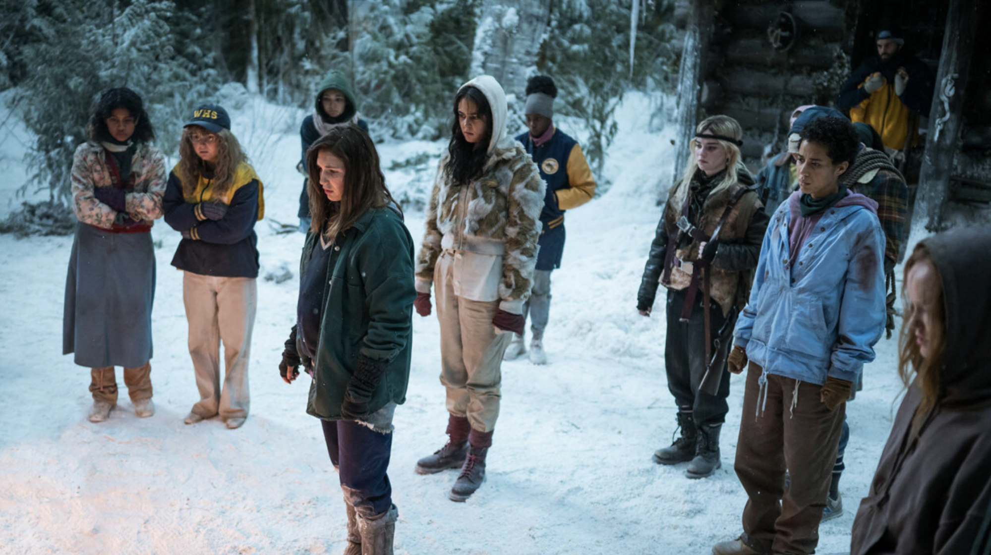 Un groupe de filles se tient dans le désert enneigé à l'extérieur d'une cabane.