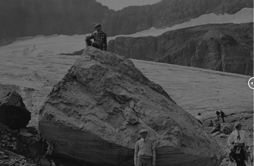 un homme assis sur un rocher observe un glacier
