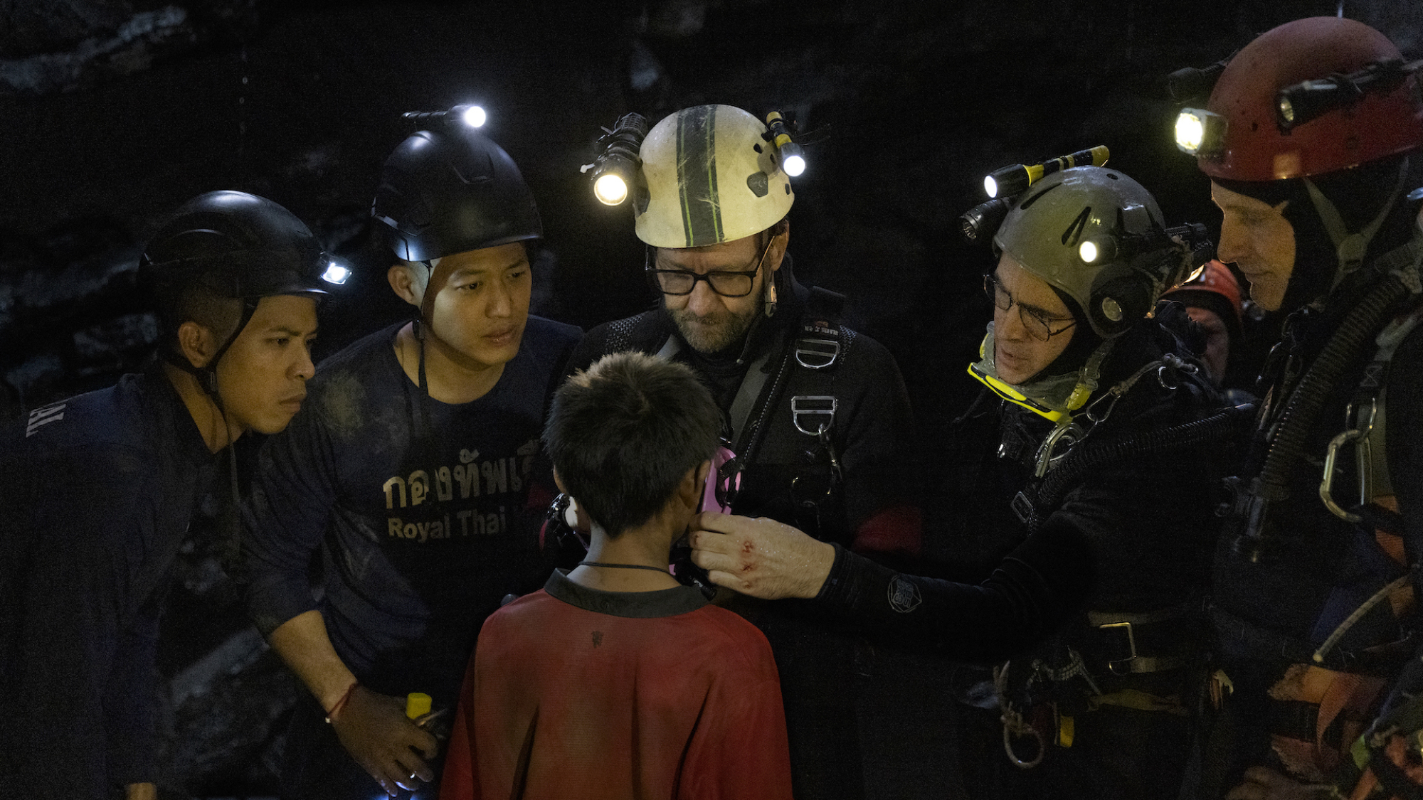 Un groupe de plongeurs munis de lampes frontales se tient avec un petit garçon dans une grotte.