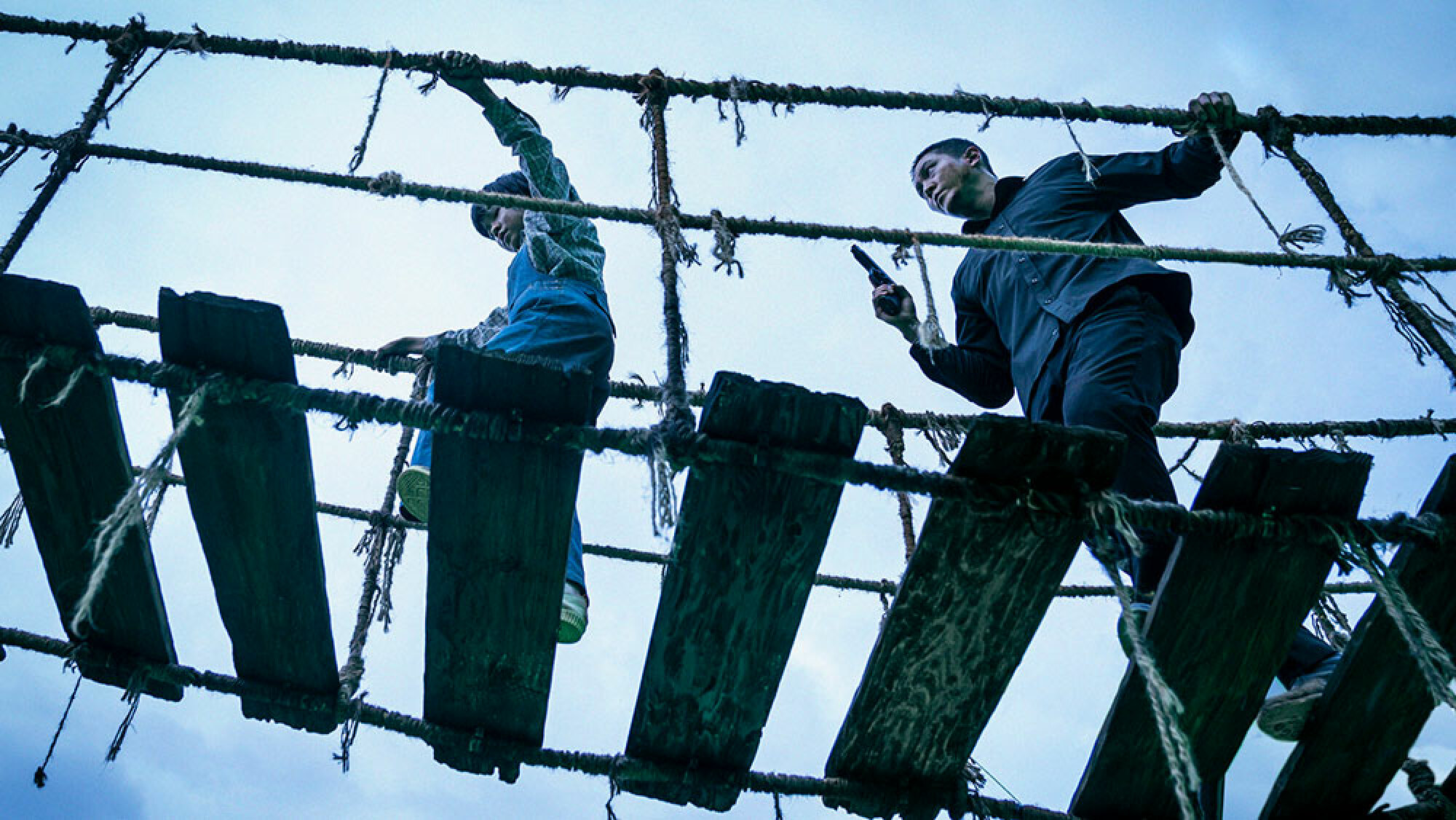 Un homme et un enfant traversent un pont de corde en décomposition.