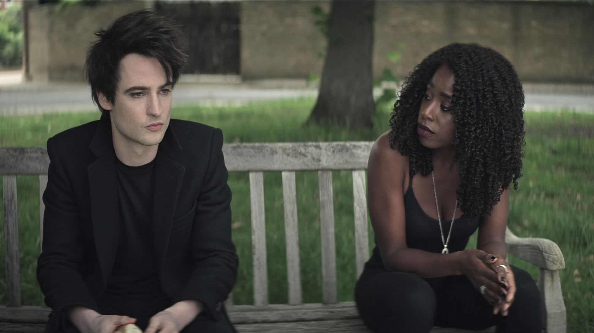 Un homme et une femme vêtus de noir sont assis sur un banc de parc.