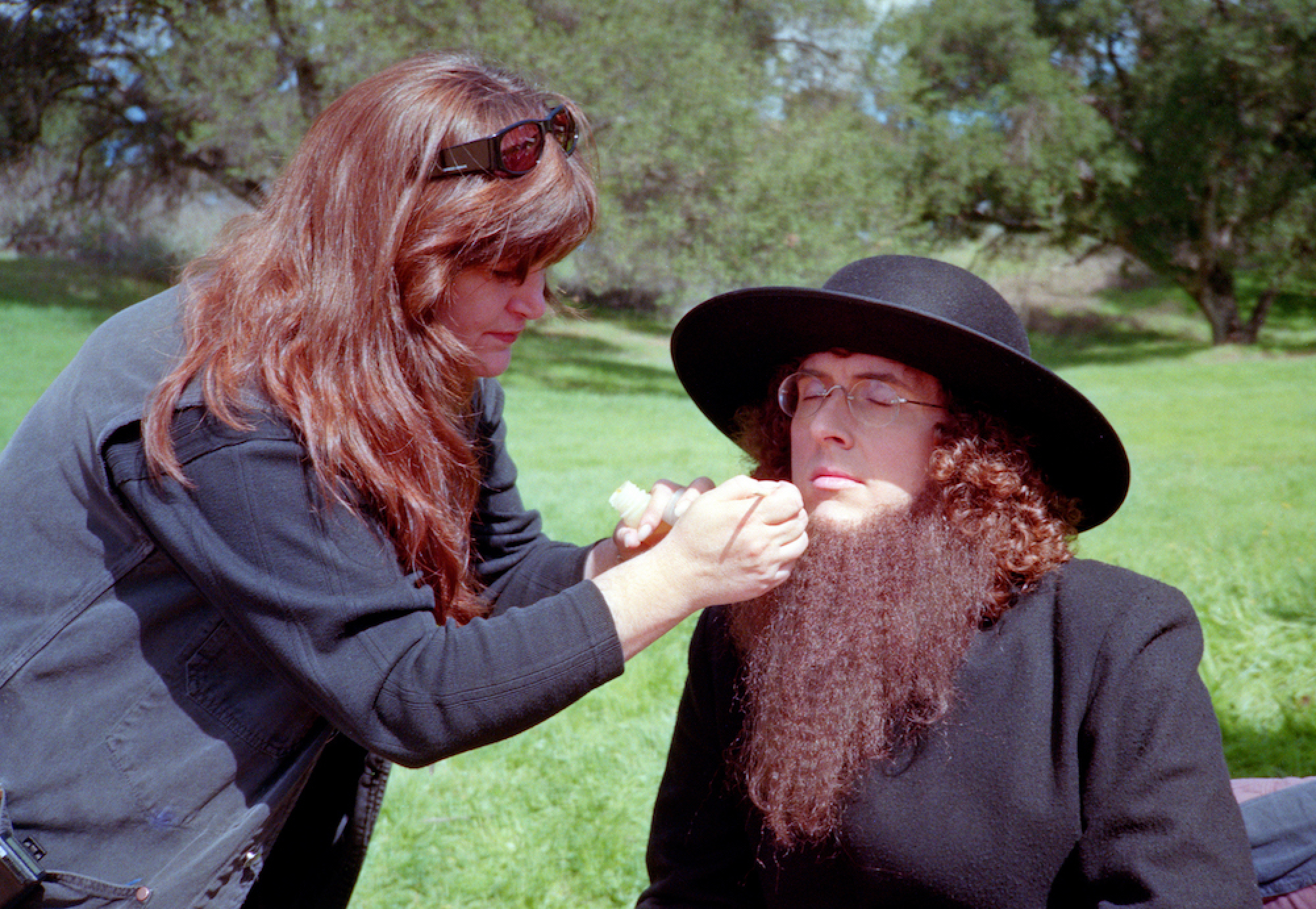 Une maquilleuse ajuste la barbe d'un homme vêtu de noir et coiffé d'un chapeau Amish noir.