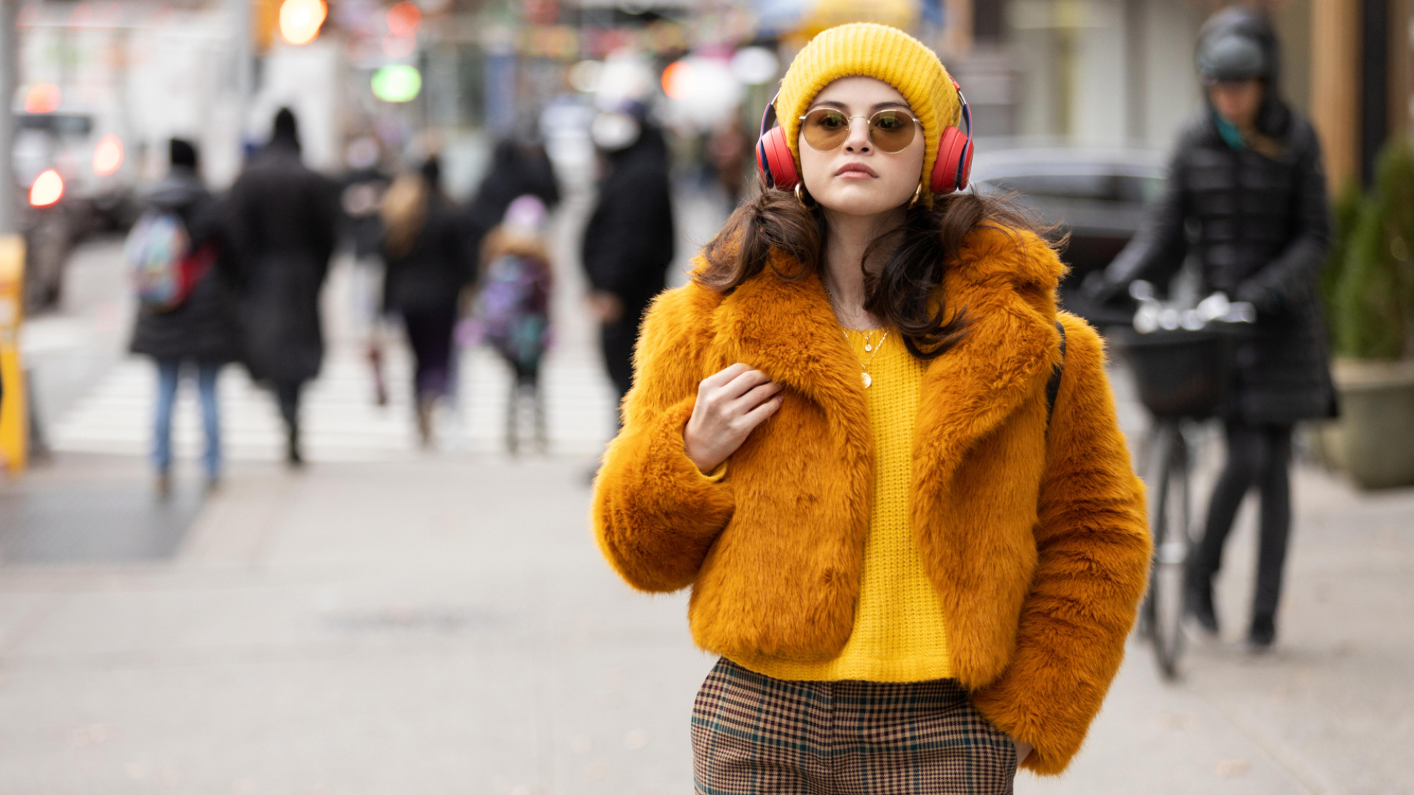 Une jeune femme dans un pull moutarde et une veste moelleuse avec des écouteurs et un bonnet assortis à New York.