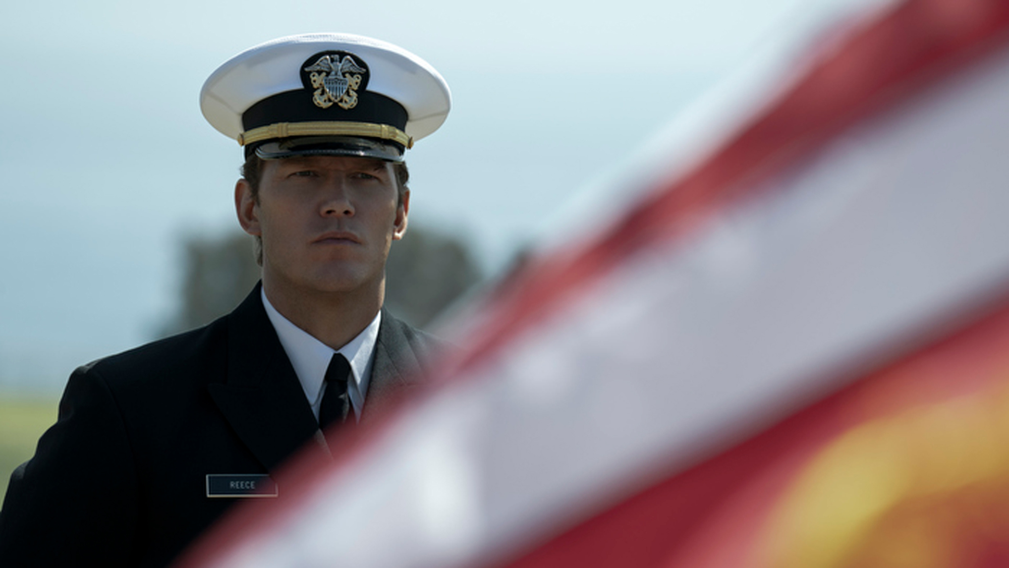 Un homme en uniforme militaire se tient à côté d'un drapeau américain.