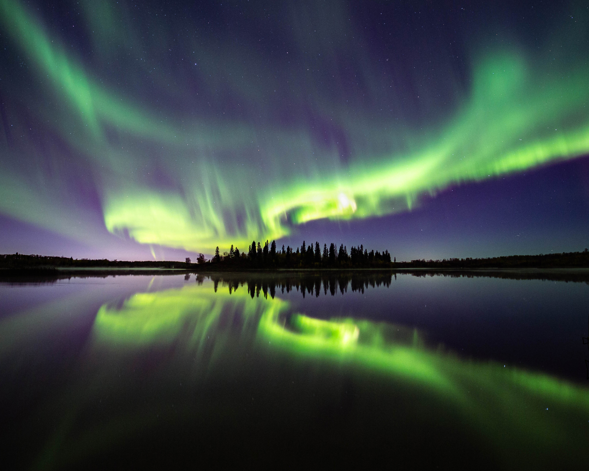 Les aurores boréales se reflètent dans les eaux calmes d'un lac en Alberta, au Canada.